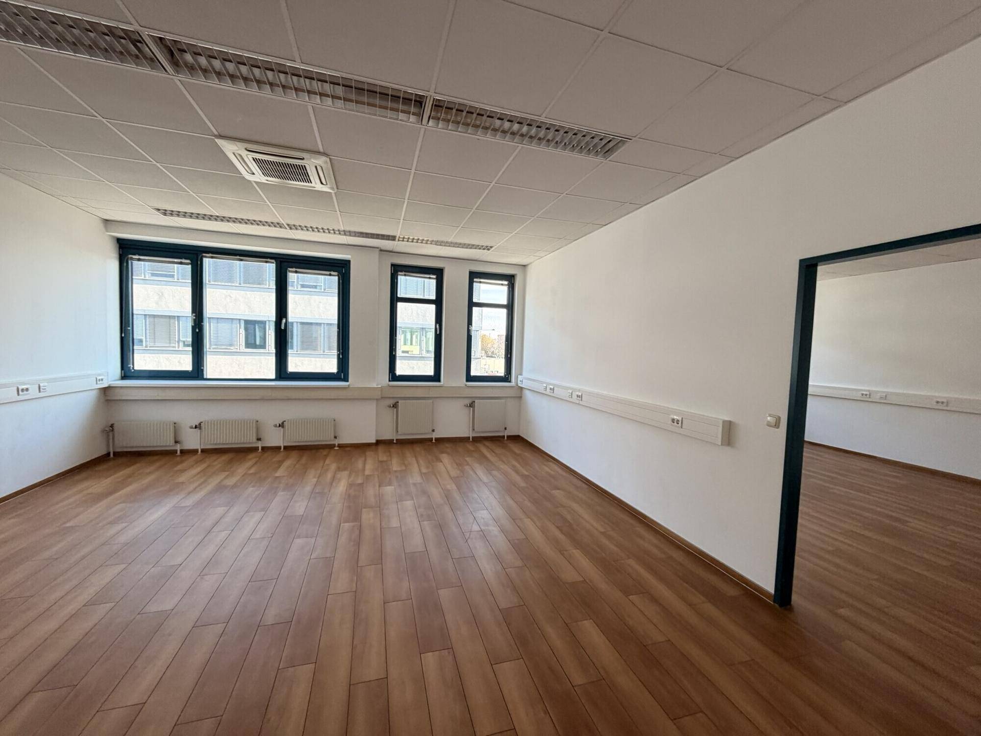 Heller Büroraum mit Holzboden, weißen Wänden und mehreren Fenstern, bereit zur Einrichtung.