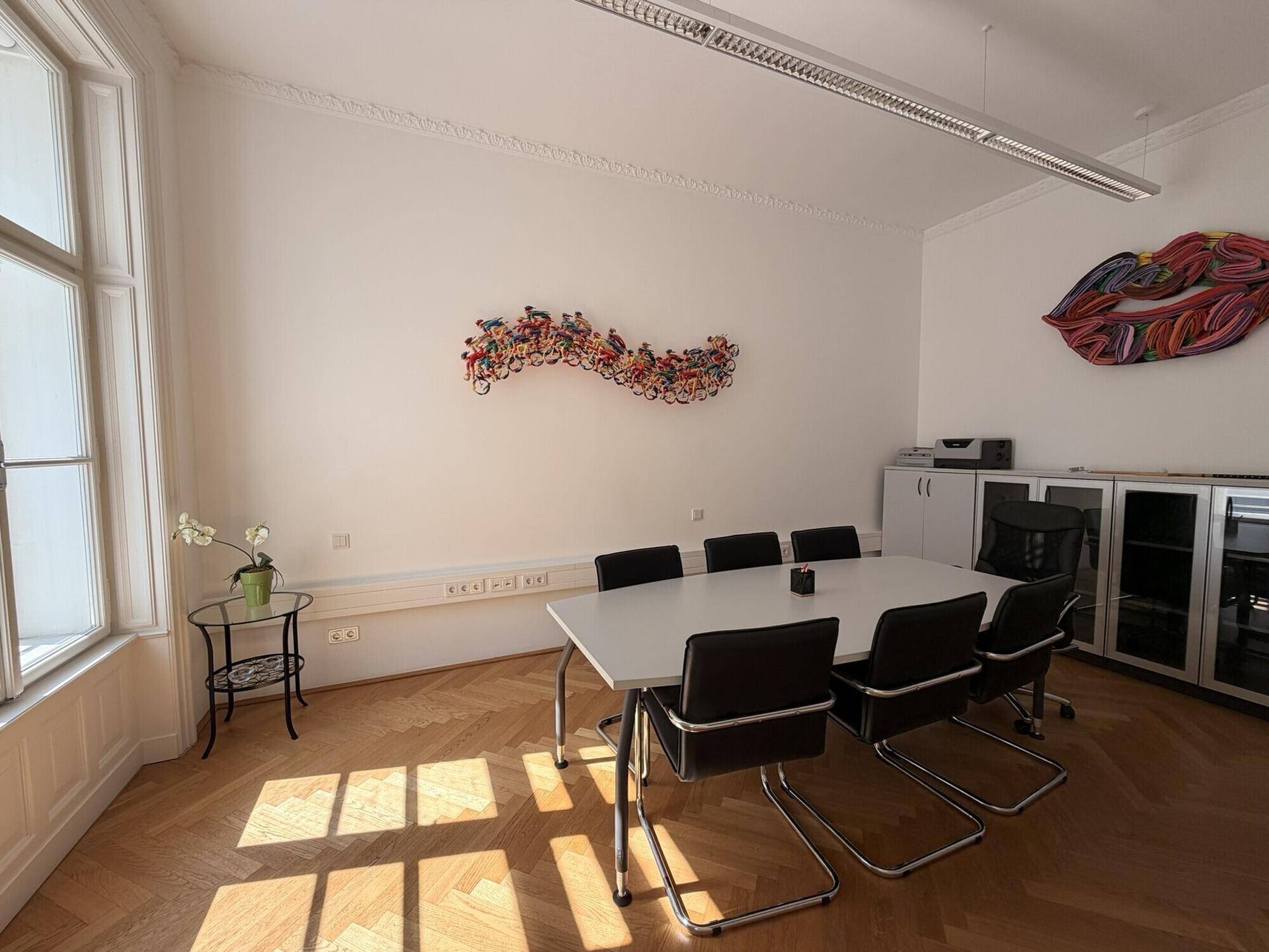 Moderner Konferenzraum mit großem Tisch, Stühlen und Kunstwerken an den weißen Wänden.