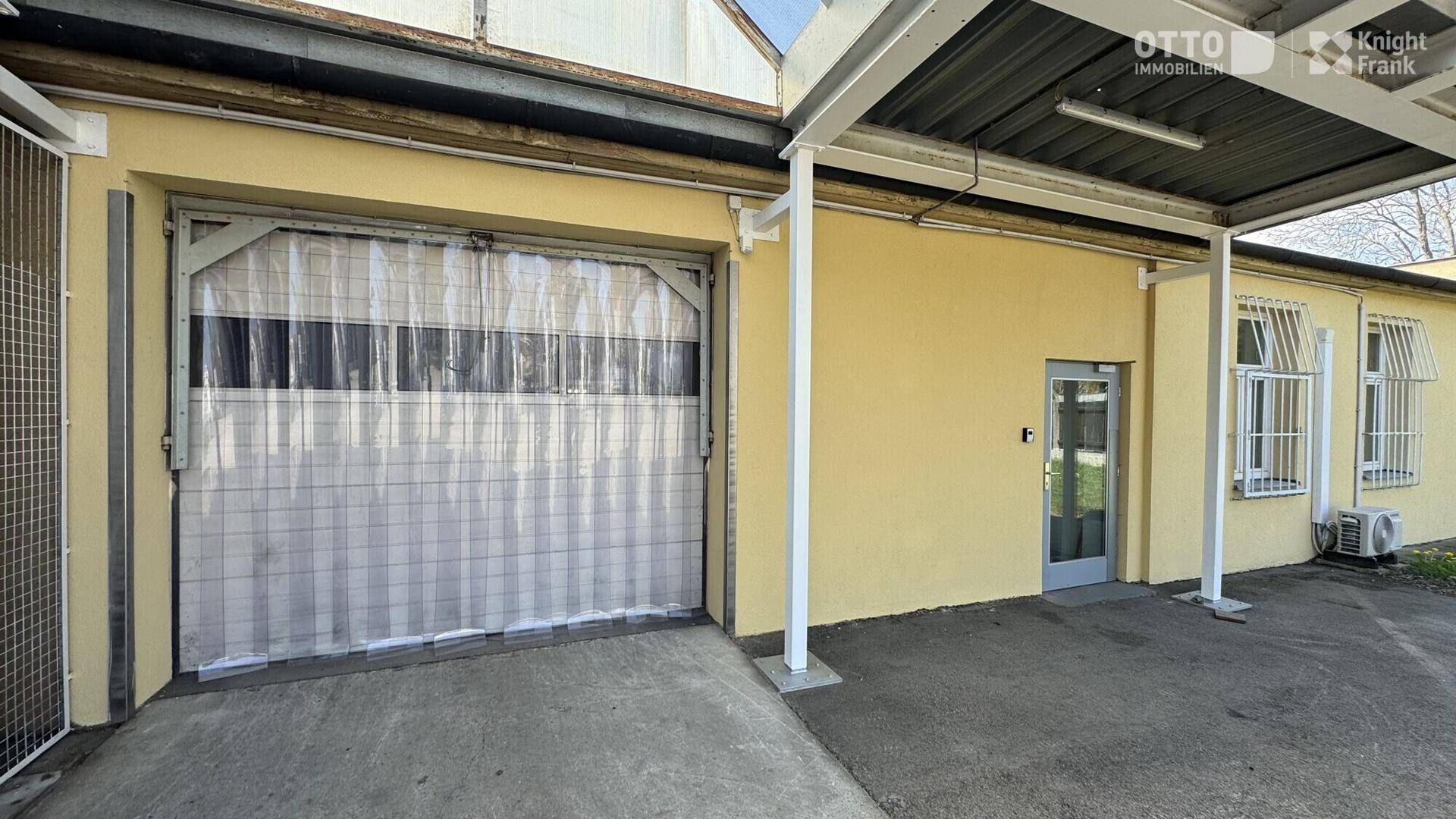 Nahaufnahme eines Garagentors mit transparentem Vorhang und angrenzendem Carport vor einem gelben Gebäude.