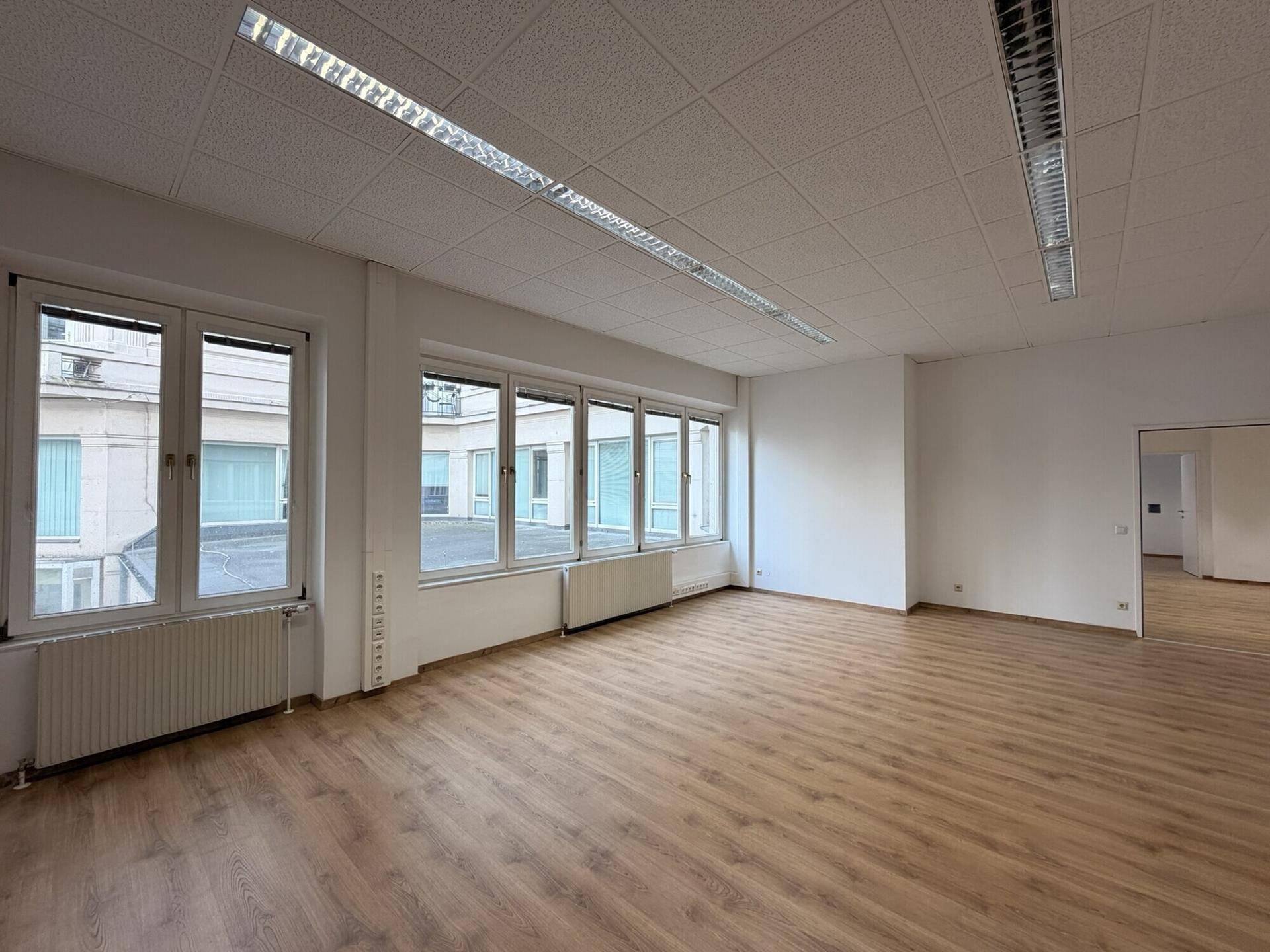 Geräumiges Büro mit Laminatboden, großen Fenstern und Blick auf einen ruhigen Innenhof.
