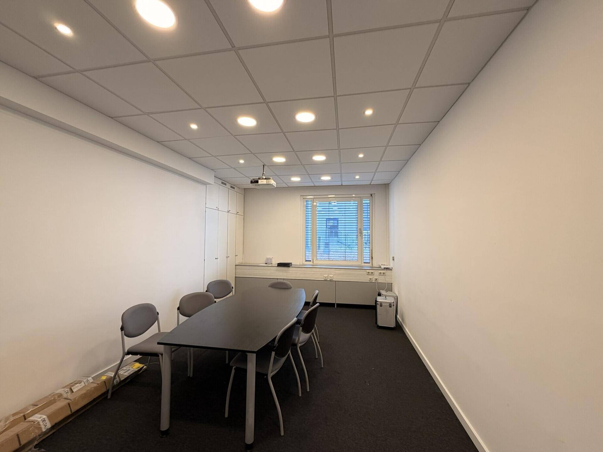 Konferenzraum mit großem Tisch, Stühlen, Beamer und Fenster, ideal für Besprechungen.