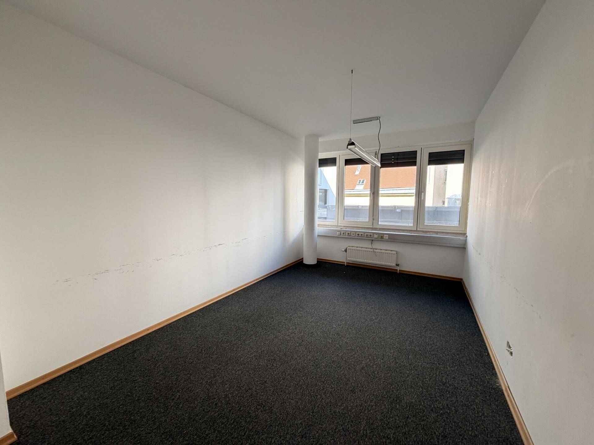 Einfaches Büro mit Teppichboden und großen Fenstern, bietet viel Tageslicht.