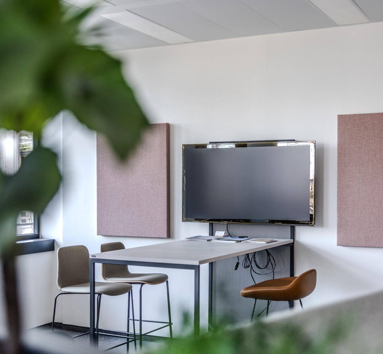Moderner Besprechungsbereich im Büro mit Wandfernseher, schallabsorbierenden Paneelen und minimalistischen Möbeln.
