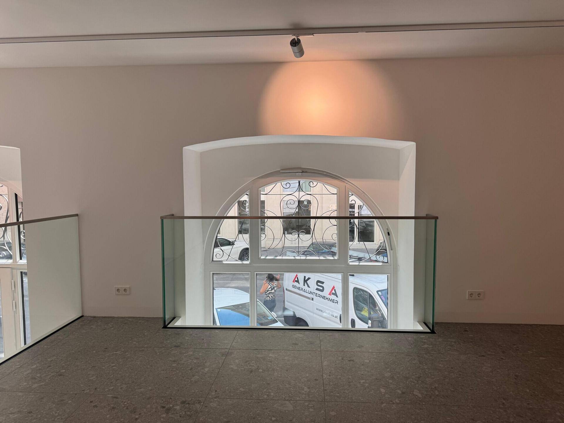 Blick von der Galerie auf die großen Bogenfenster im Erdgeschoss, die viel Tageslicht hereinlassen und eine helle Atmosphäre schaffen.