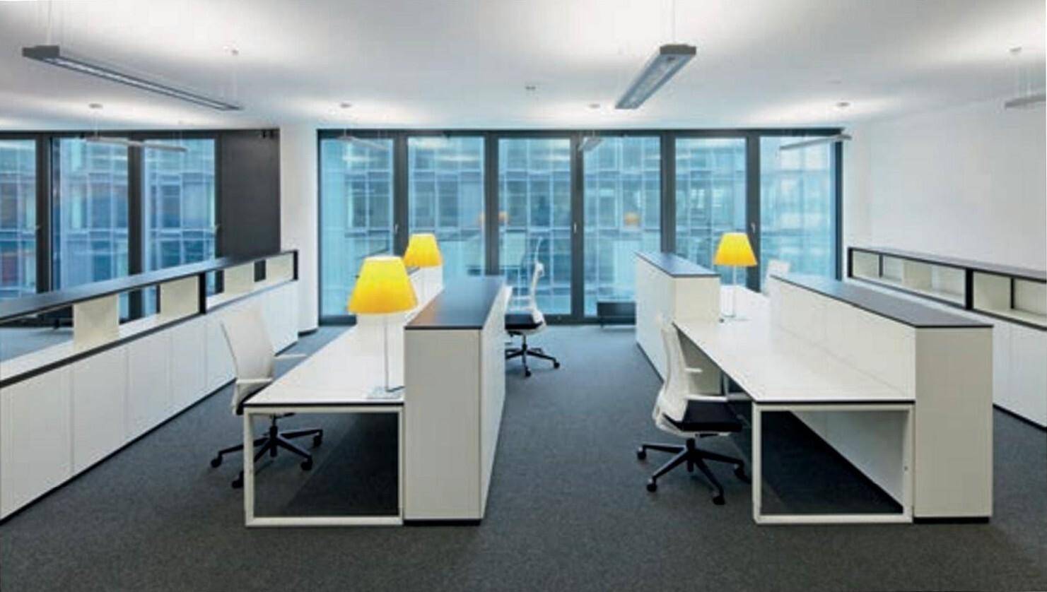 Modern eingerichteter Bürobereich mit mehreren Arbeitsplätzen, Teppichboden und großen Fenstern mit Blick nach draußen.