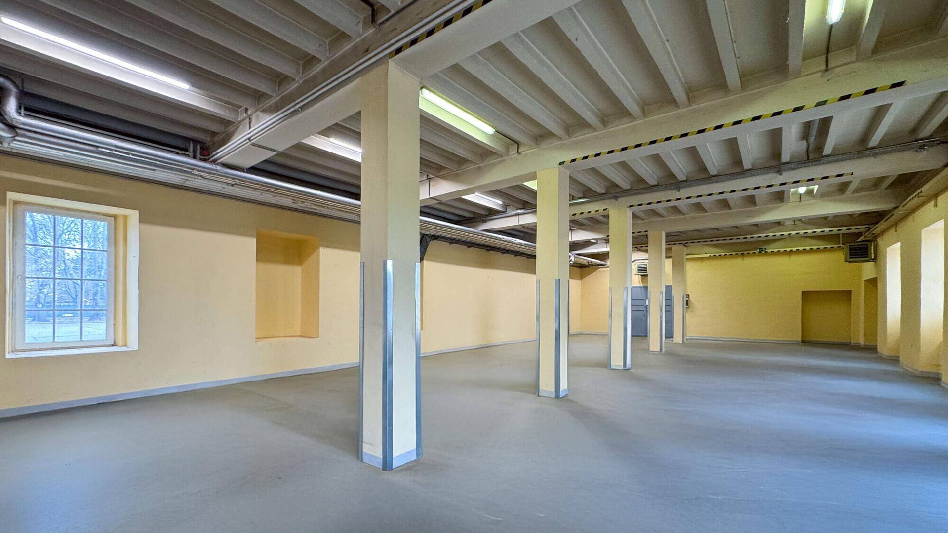 Großer, offener Raum mit gelben Wänden, vielen Säulen, hohen Decken und Betonboden, ideal für Lagerung.
