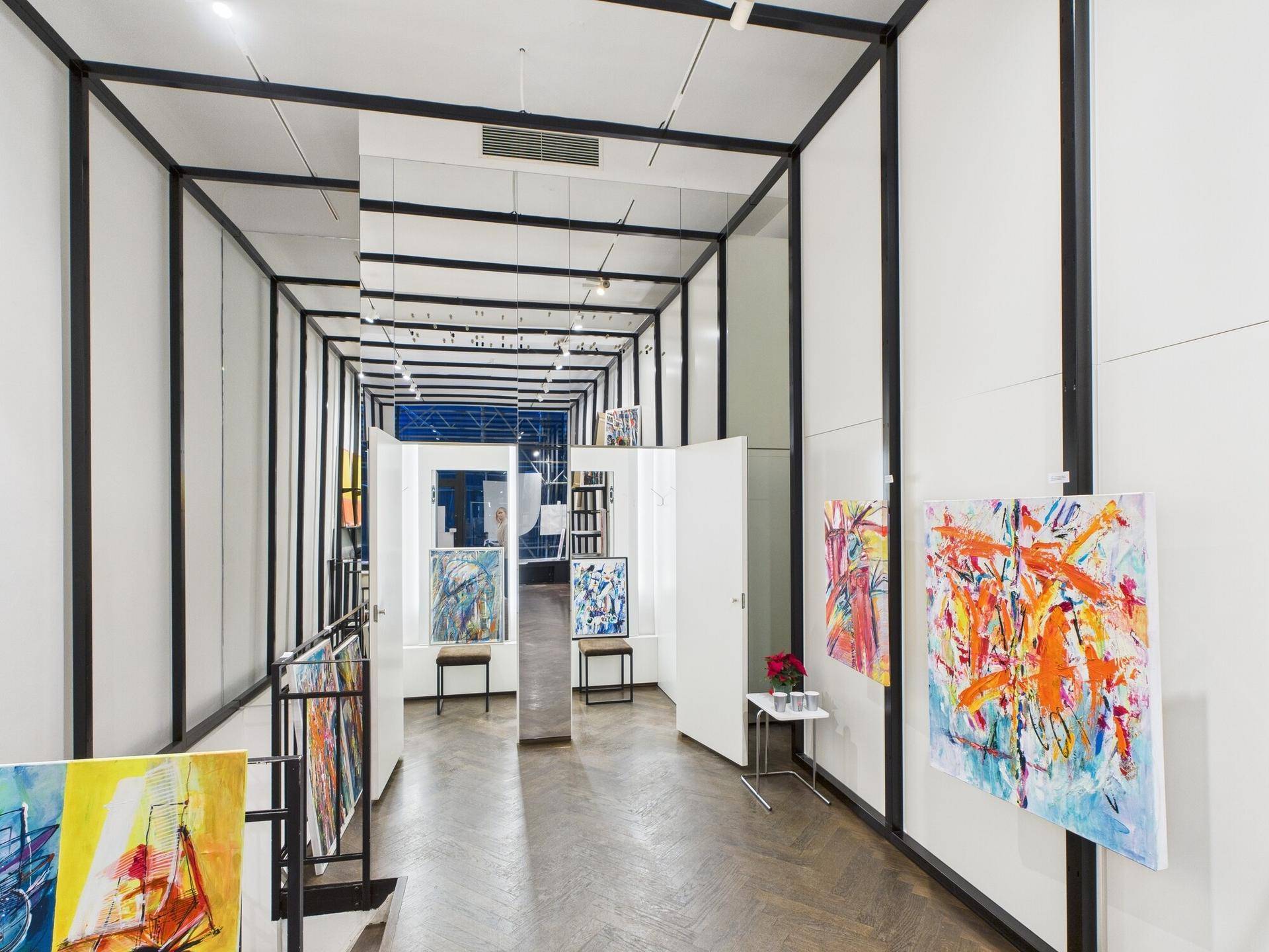 Langer Galeriekeller mit Kunstausstellung, Fischgrätparkett und reflektierenden Oberflächen, die Tiefe schaffen.