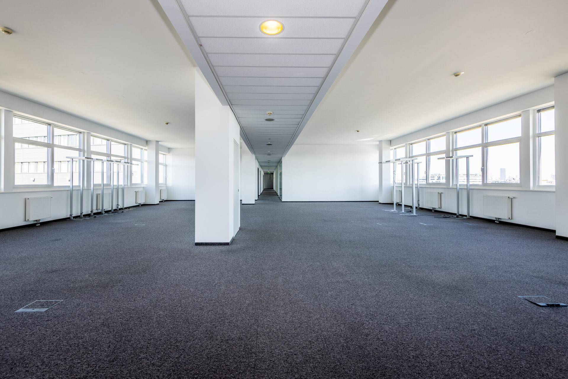 Großer, offener Bürobereich mit Teppichboden, vielen Fenstern und Blick auf die Stadt.