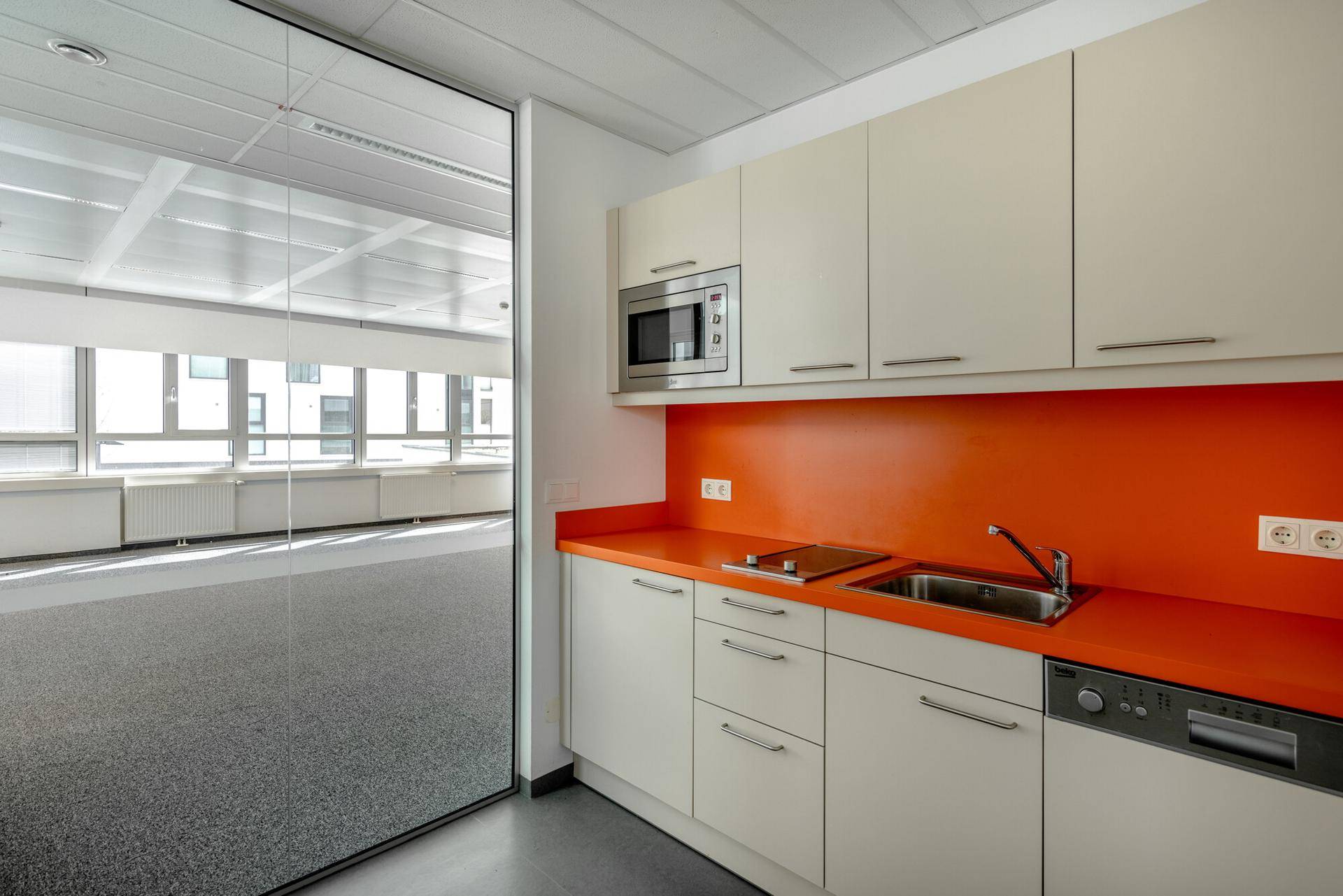Kleine Teeküche mit beigen Schränken, orangefarbener Arbeitsplatte und integrierter Mikrowelle.
