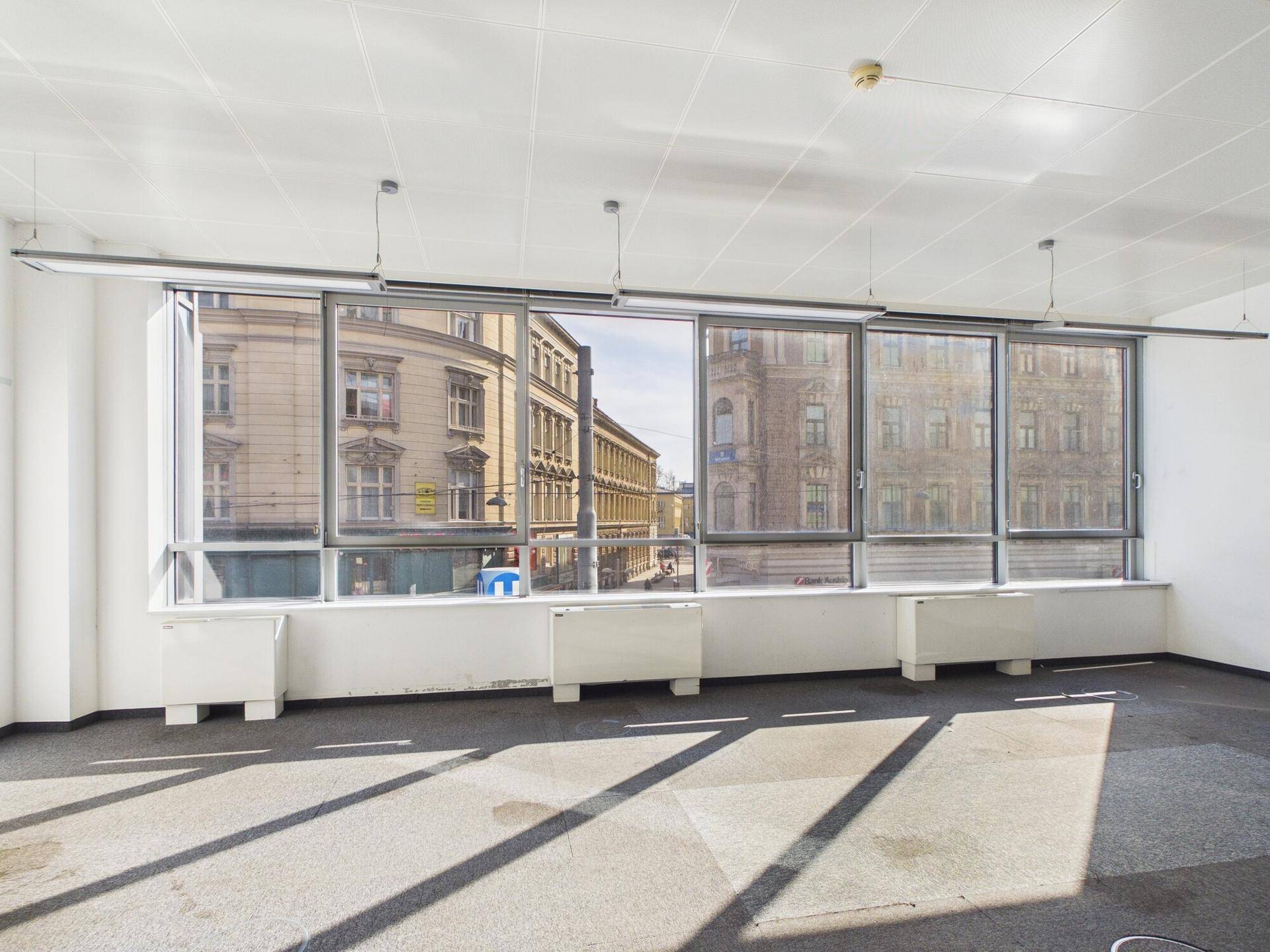 Heller Büroraum mit langer Fensterfront, die viel Sonnenlicht und einen urbanen Ausblick bietet.