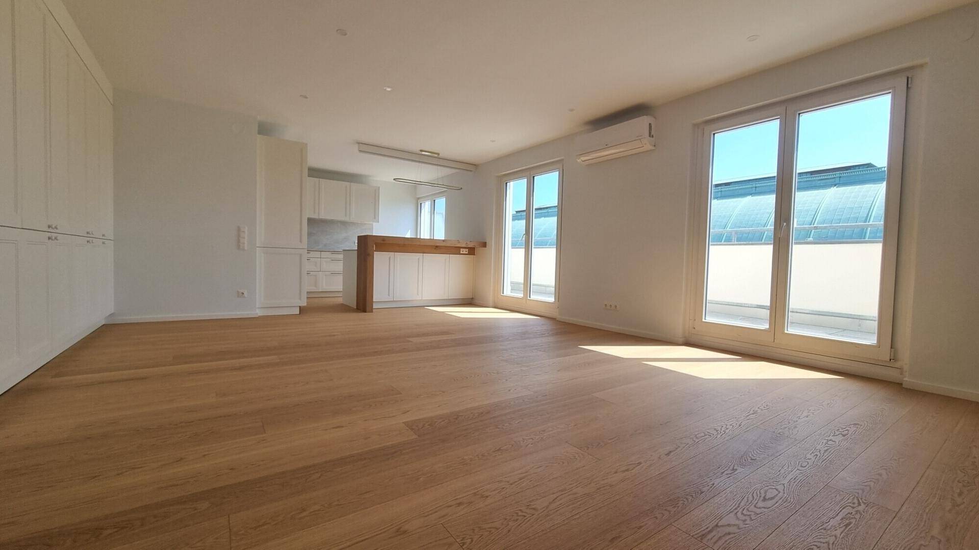 Helles, offenes Wohnzimmer mit Holzboden, Einbauschränken und großen Fenstern.
