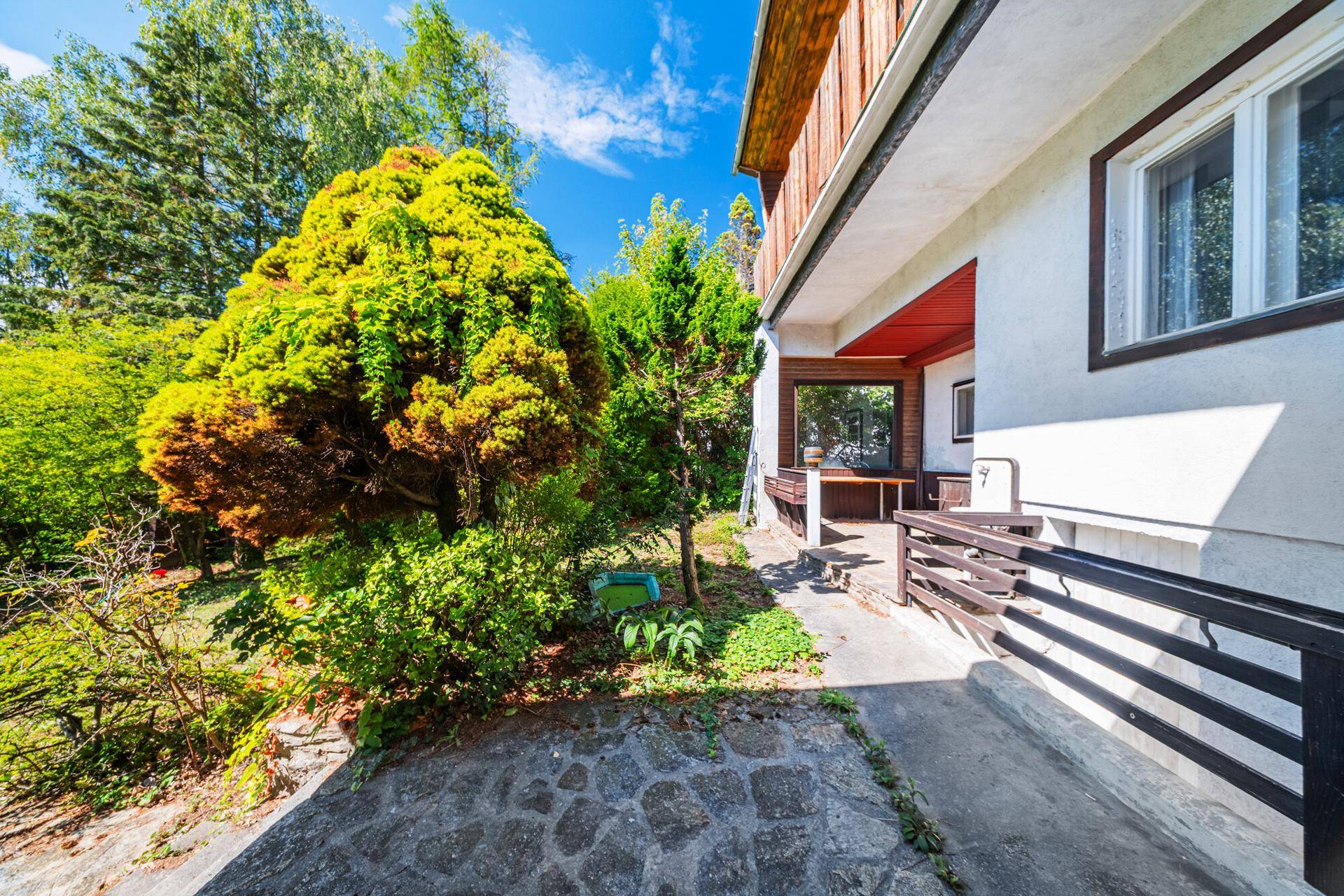 Seitlicher Gartenbereich mit gepflastertem Weg und Zugang zur überdachten Terrasse des Hauses.