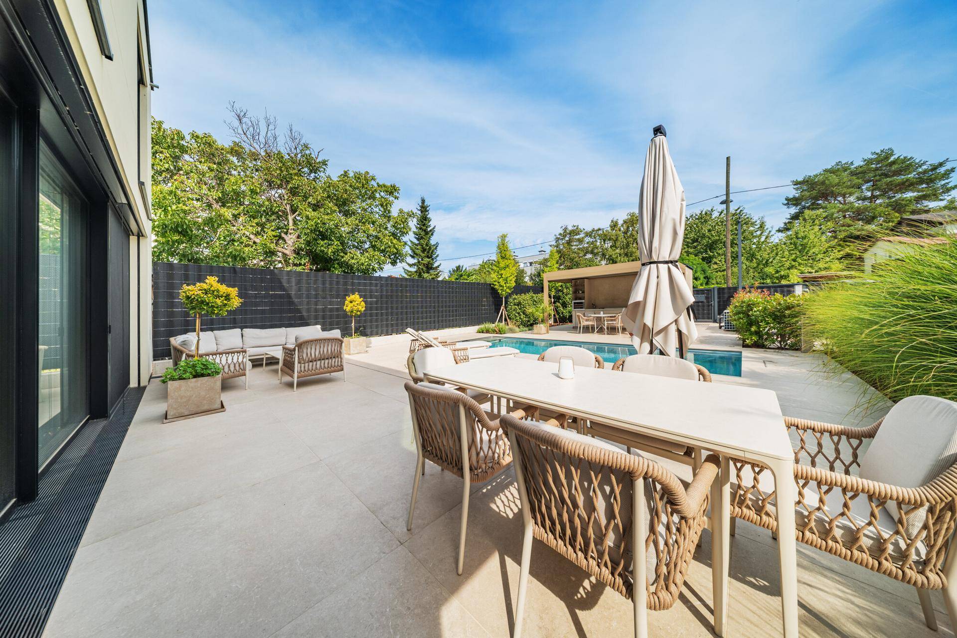 Geräumige Terrasse mit Esstisch und Lounge-Möbeln, umgeben von Grün und mit Blick auf den Pool.