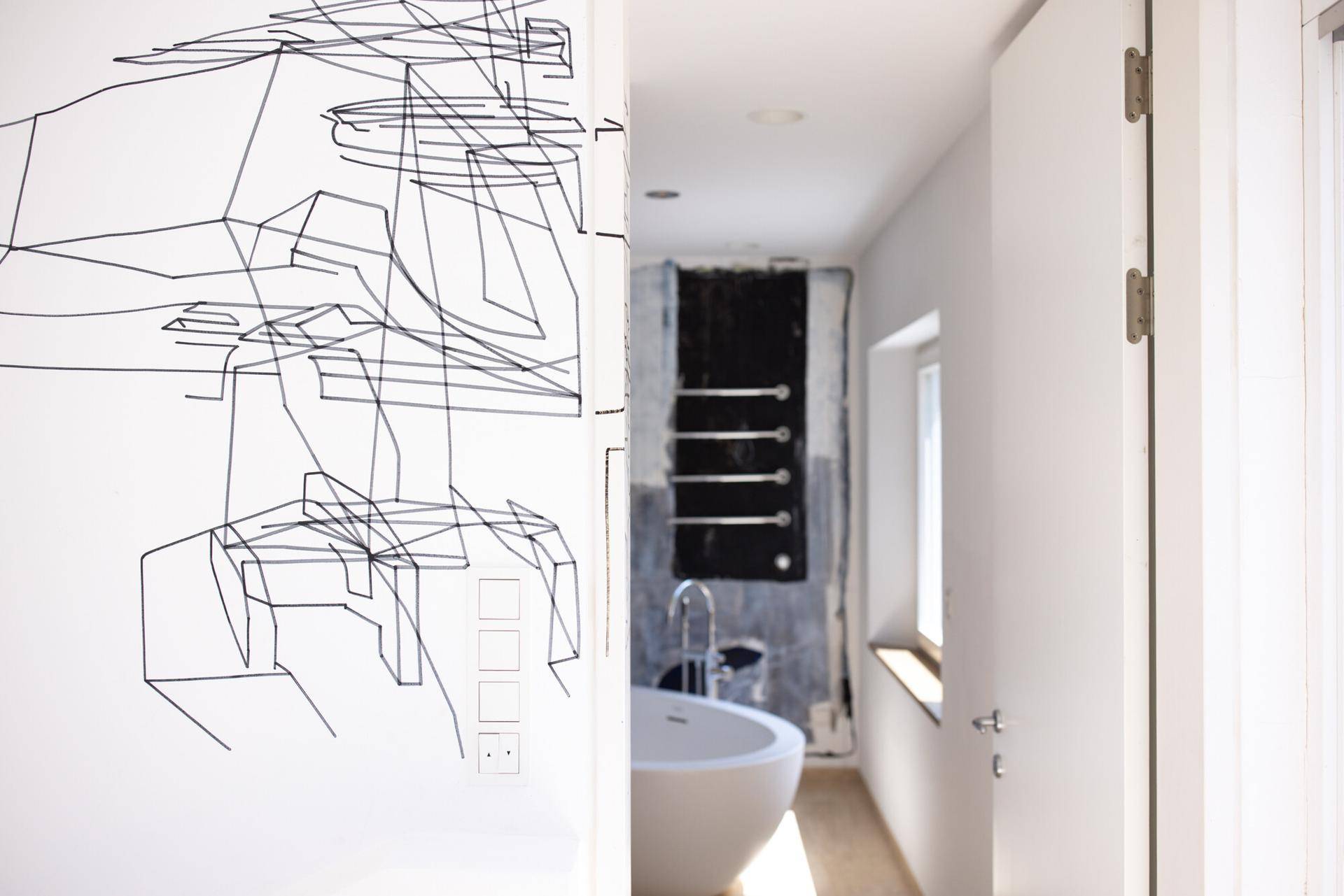 Blick vom Flur in ein modernes Badezimmer mit freistehender Badewanne und Handtuchhalter.