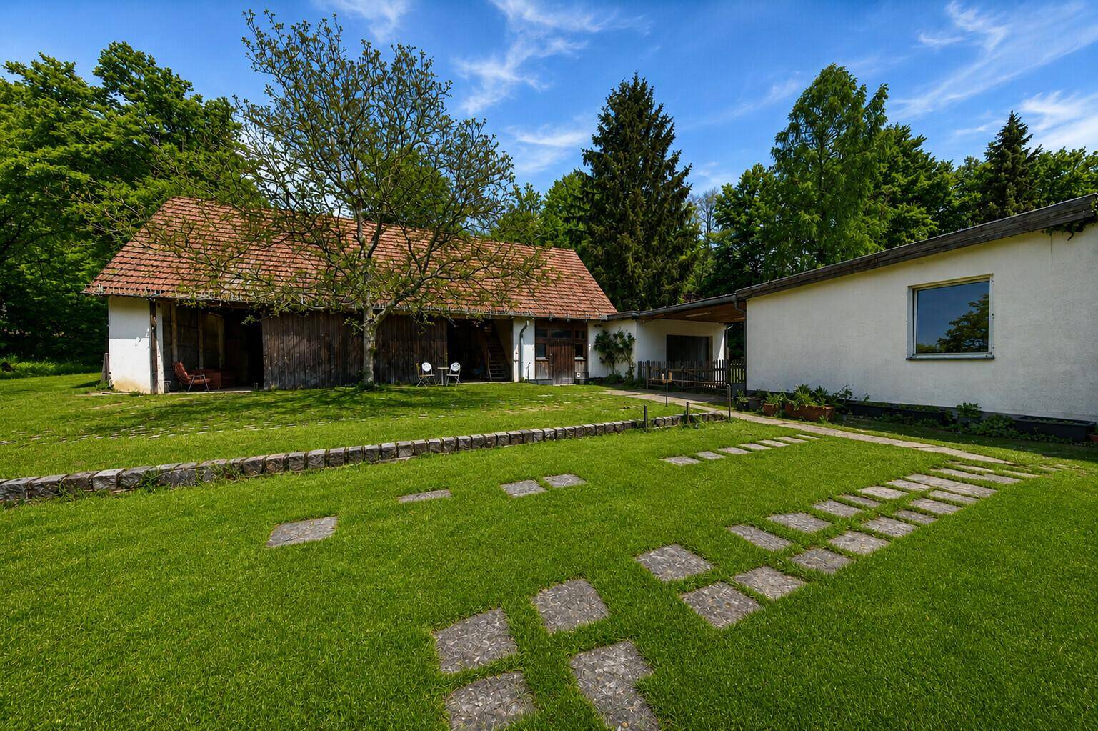 Zwei Gebäude mit großem Rasen und Steinplatten, umgeben von Bäumen an einem sonnigen Tag.