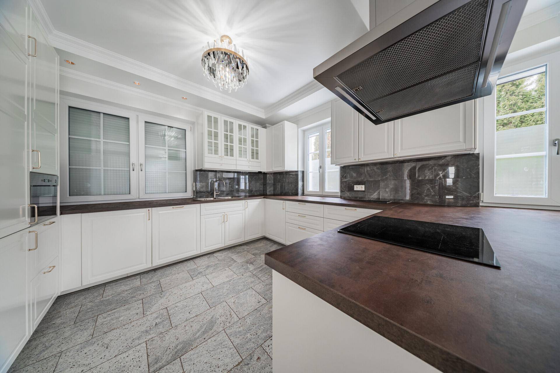 Moderne Einbauküche mit weißen Schränken, Induktionskochfeld und eleganten Arbeitsplatten.