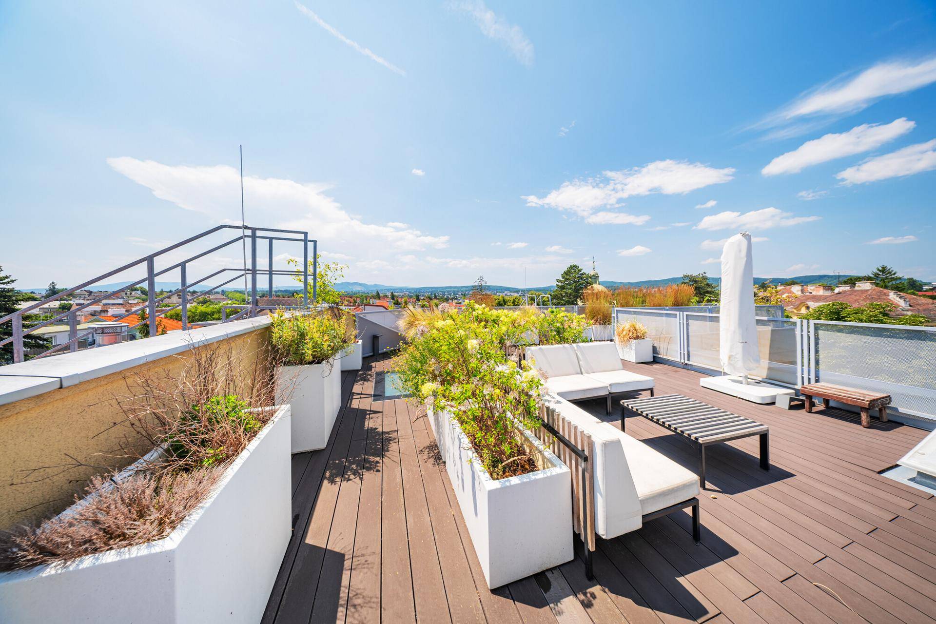 Weitläufige Dachterrasse mit Holzbelag, Pflanzen in Kübeln und einem Panoramablick über die Umgebung.