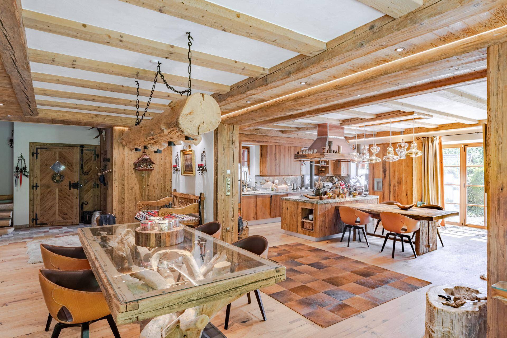 Weitläufiger Wohn- und Essbereich mit offener Küche, Holzbalken und großen Fenstern.