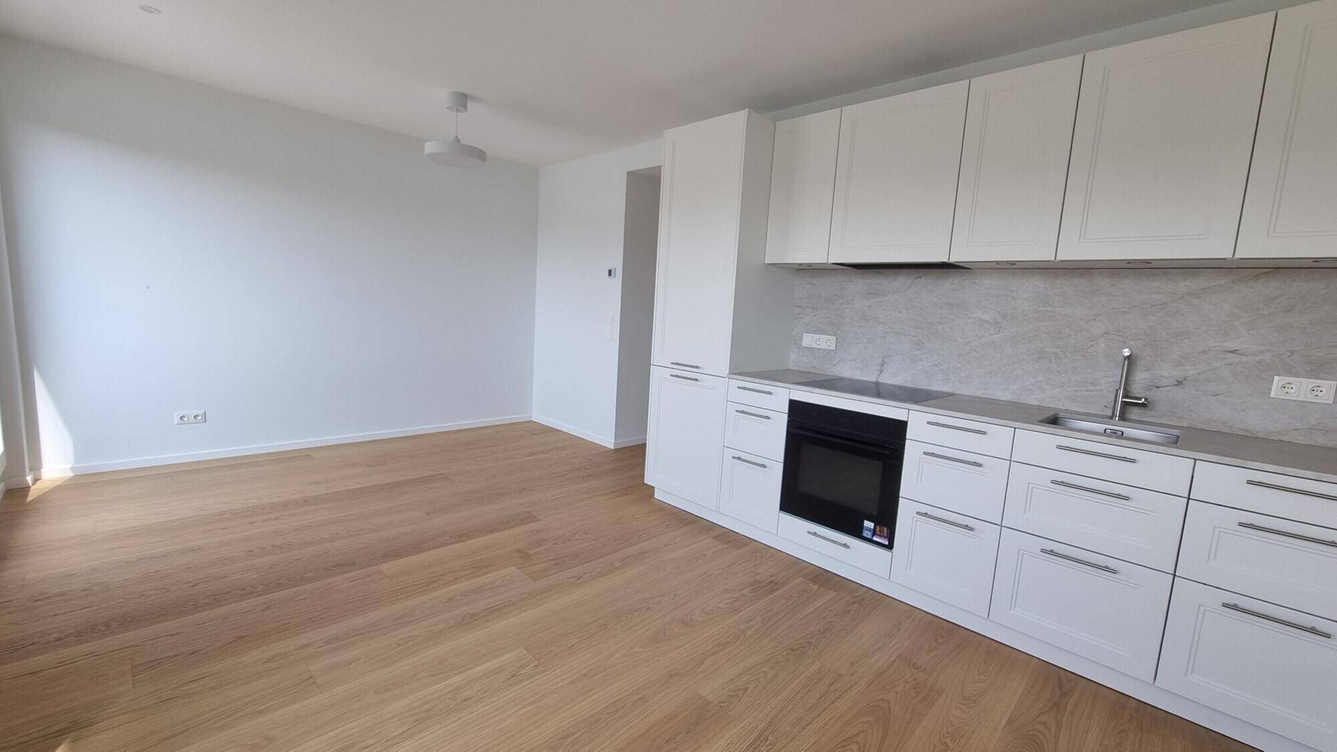 Moderne, offene Küche mit weißen Schränken und hellem Holzboden, kombiniert mit einem leeren Wohnbereich.