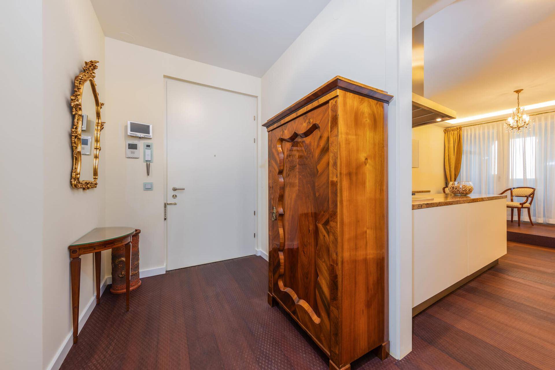 Eingangsbereich mit dunklem Holzboden, antikem Schrank und Blick in den offenen Wohnbereich.