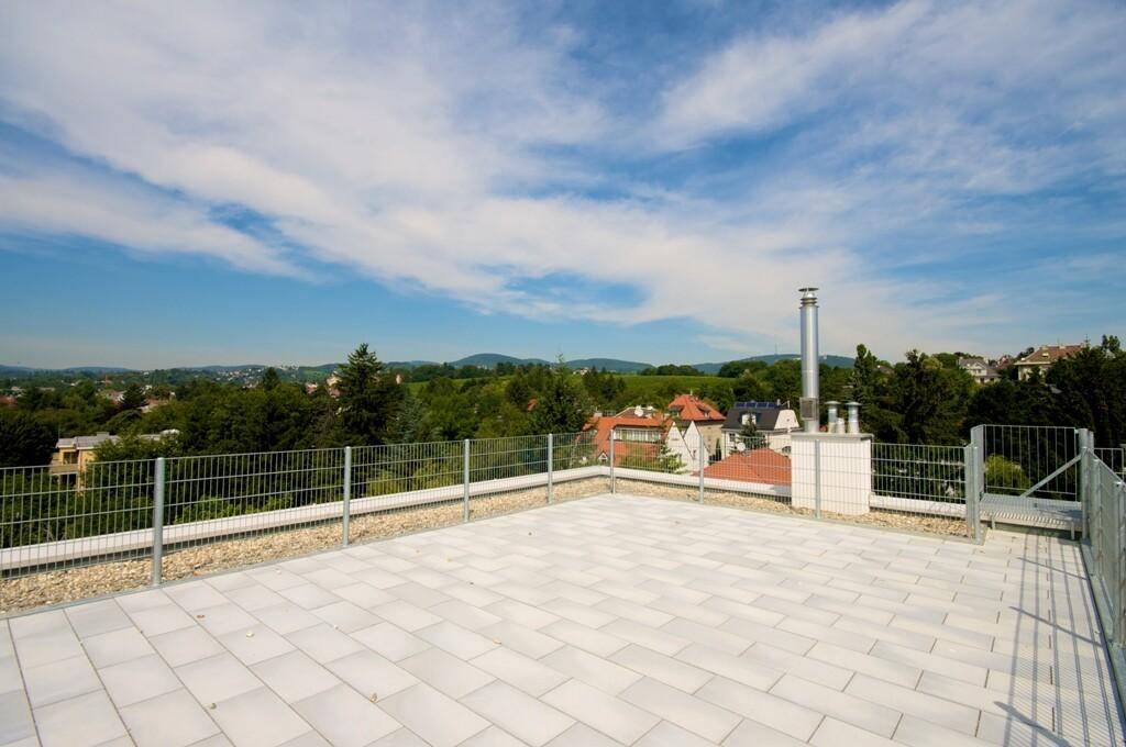 Offene Dachterrasse mit weitem Panoramablick über grüne Hügel, Bäume und Wohngebäude in der Ferne.