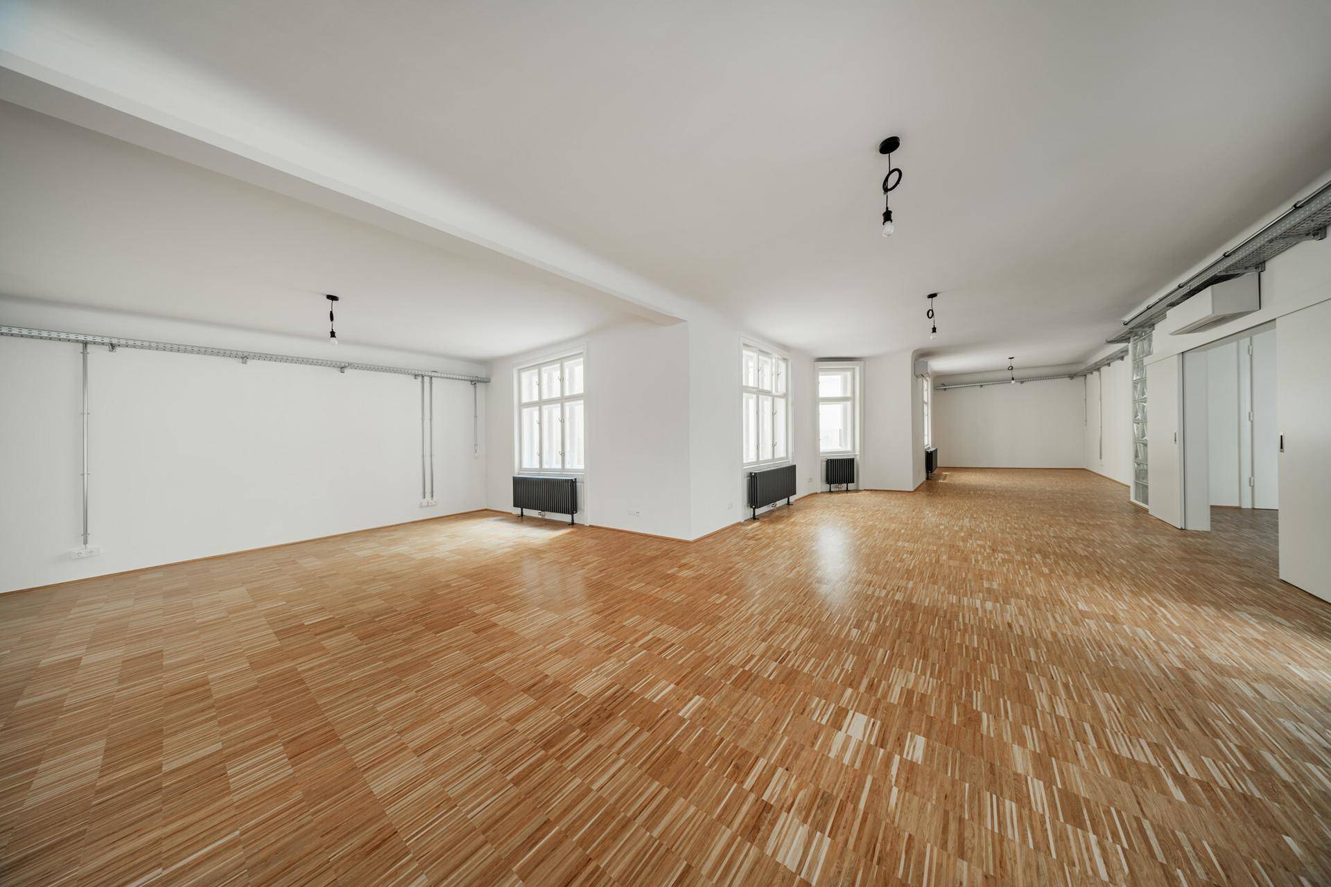 Geräumiges, helles Zimmer mit klassischem Parkettboden und mehreren Fenstern, bereit zur individuellen Gestaltung.