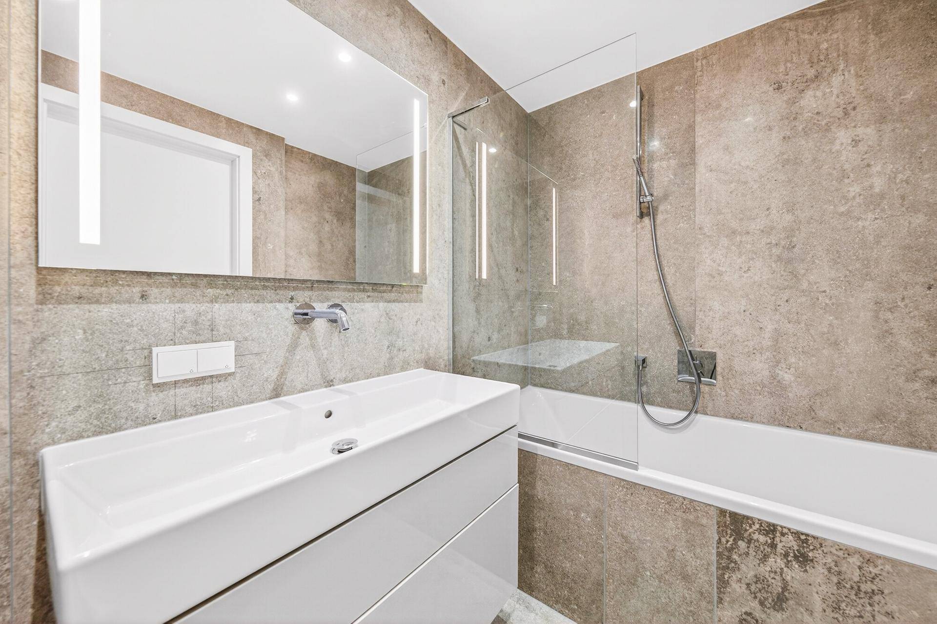 Elegantes Badezimmer mit großem Waschtisch, beleuchtetem Spiegel und Badewanne mit Duschfunktion.