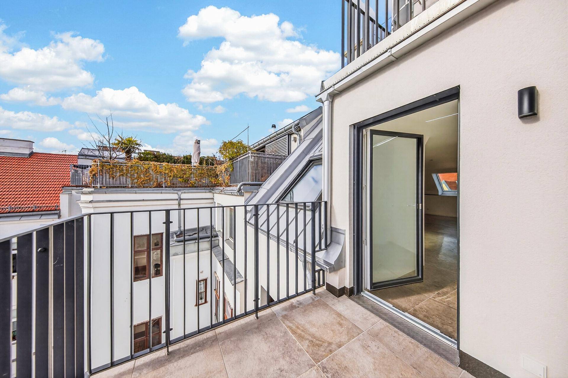 Heller Balkon mit Zugang zu einem Innenraum und Blick auf die umliegenden Dächer.