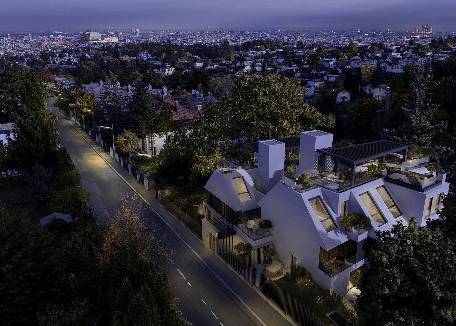 Abendliche Luftaufnahme der Wohnanlage mit beleuchteter Straße und der Stadt im Hintergrund.