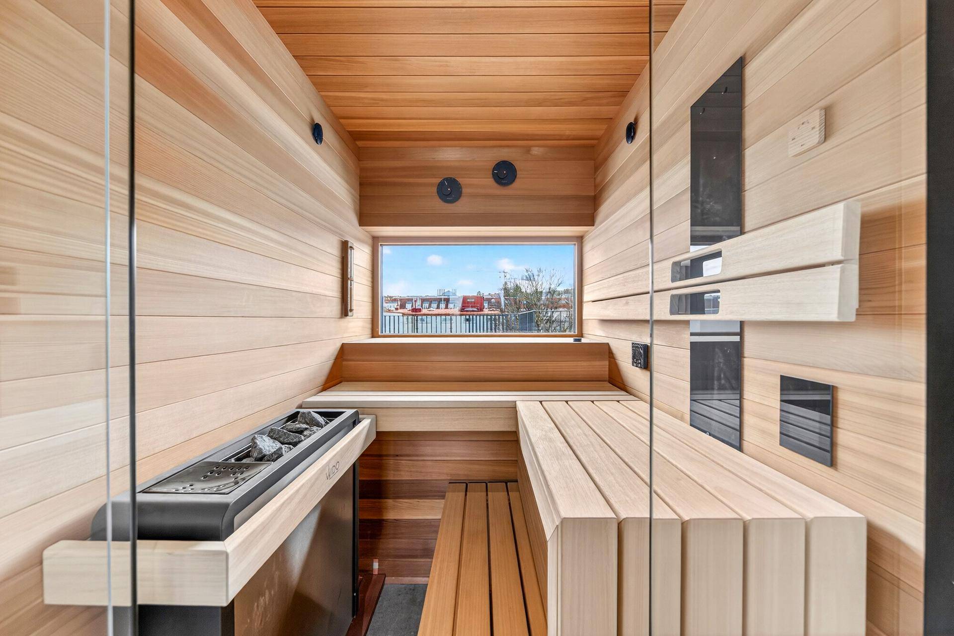 Moderne Sauna mit hellem Holz und Blick aus dem Fenster auf die umliegenden Dächer.