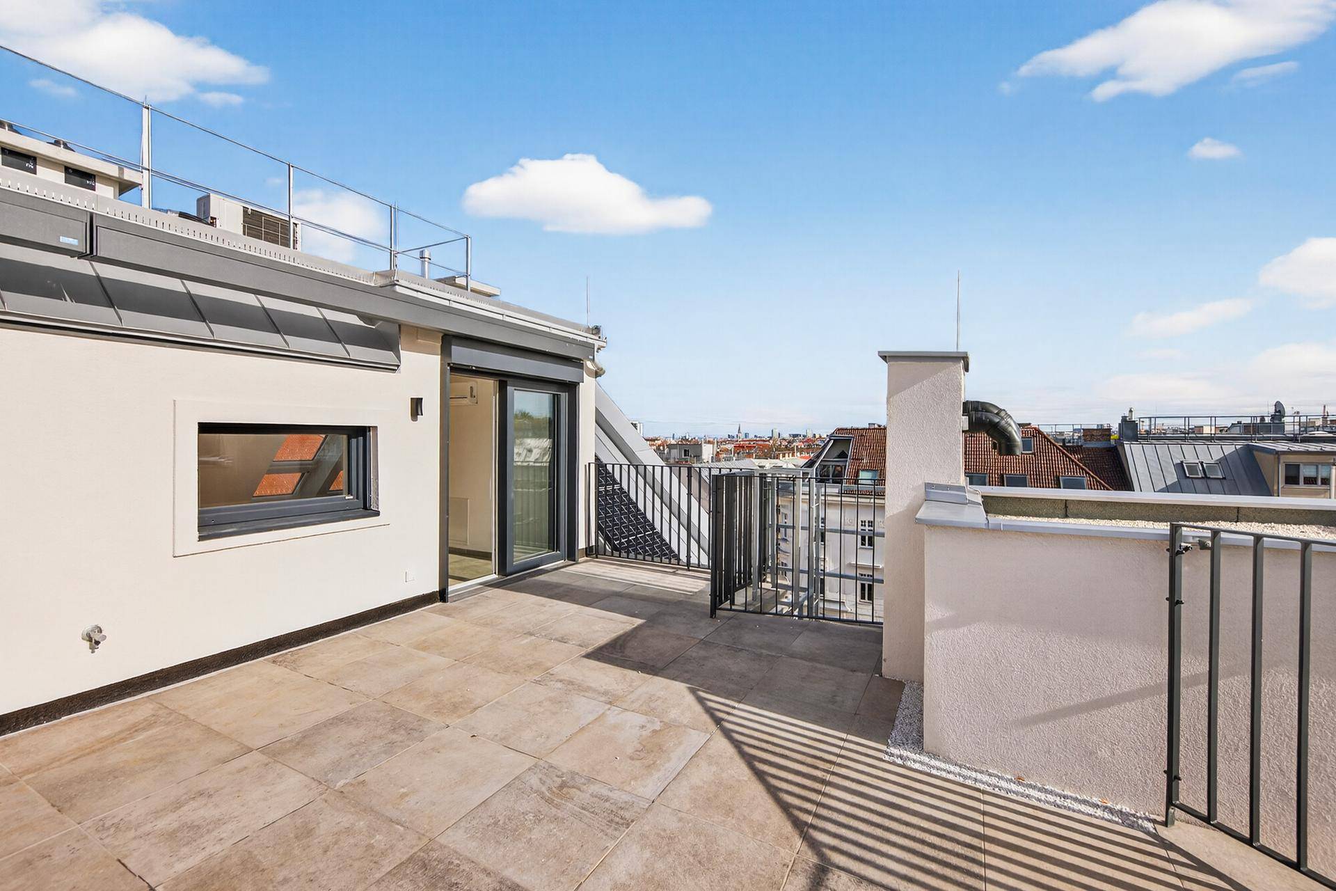 Geräumige, geflieste Dachterrasse mit Schiebetür zum Innenbereich und weitem Stadtblick.