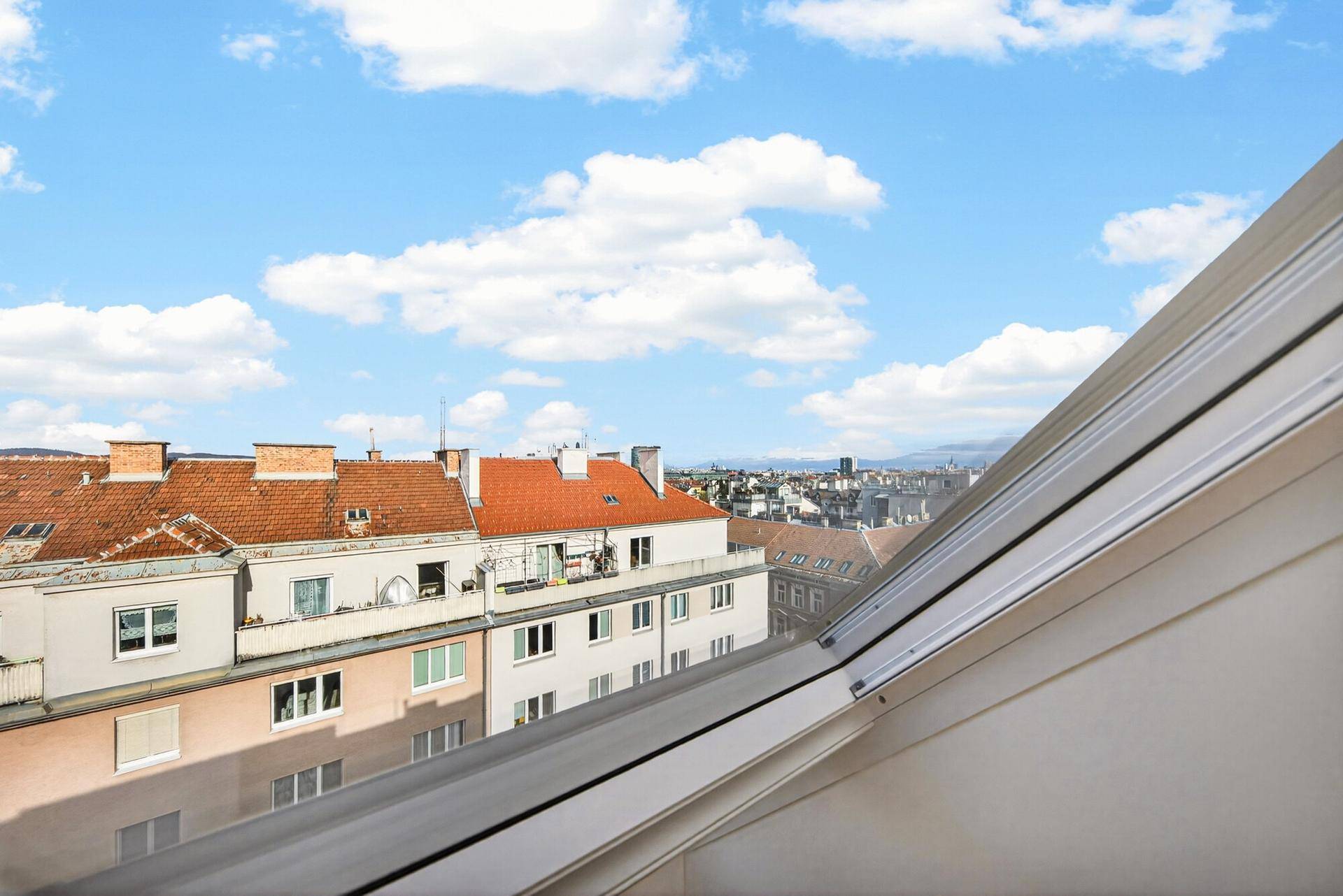 Weitblick aus einem Dachfenster über die Dächer der Stadt bis zum Horizont.