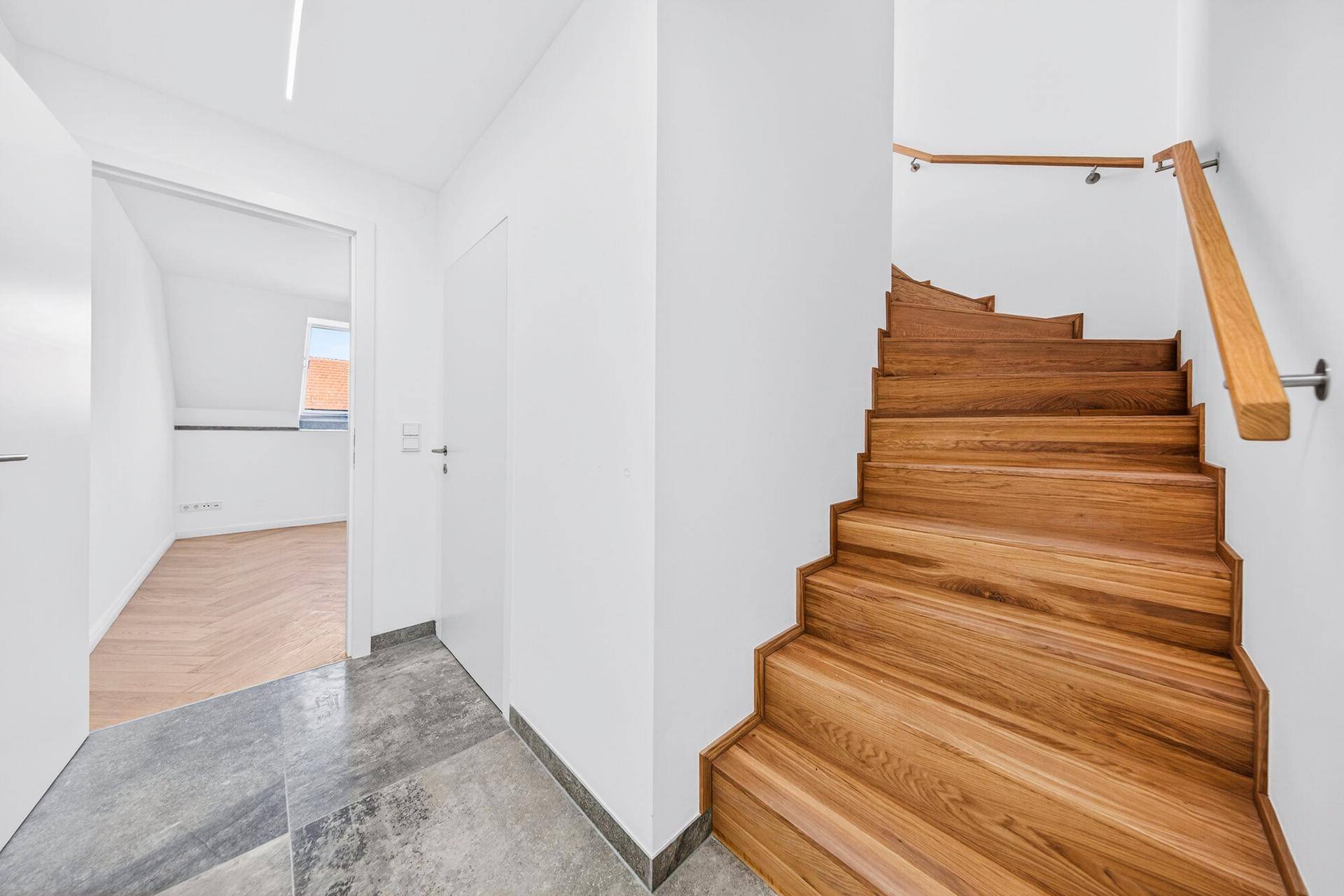 Heller Flur mit eleganter Holztreppe und einer Kombination aus Fliesen- und Parkettboden.