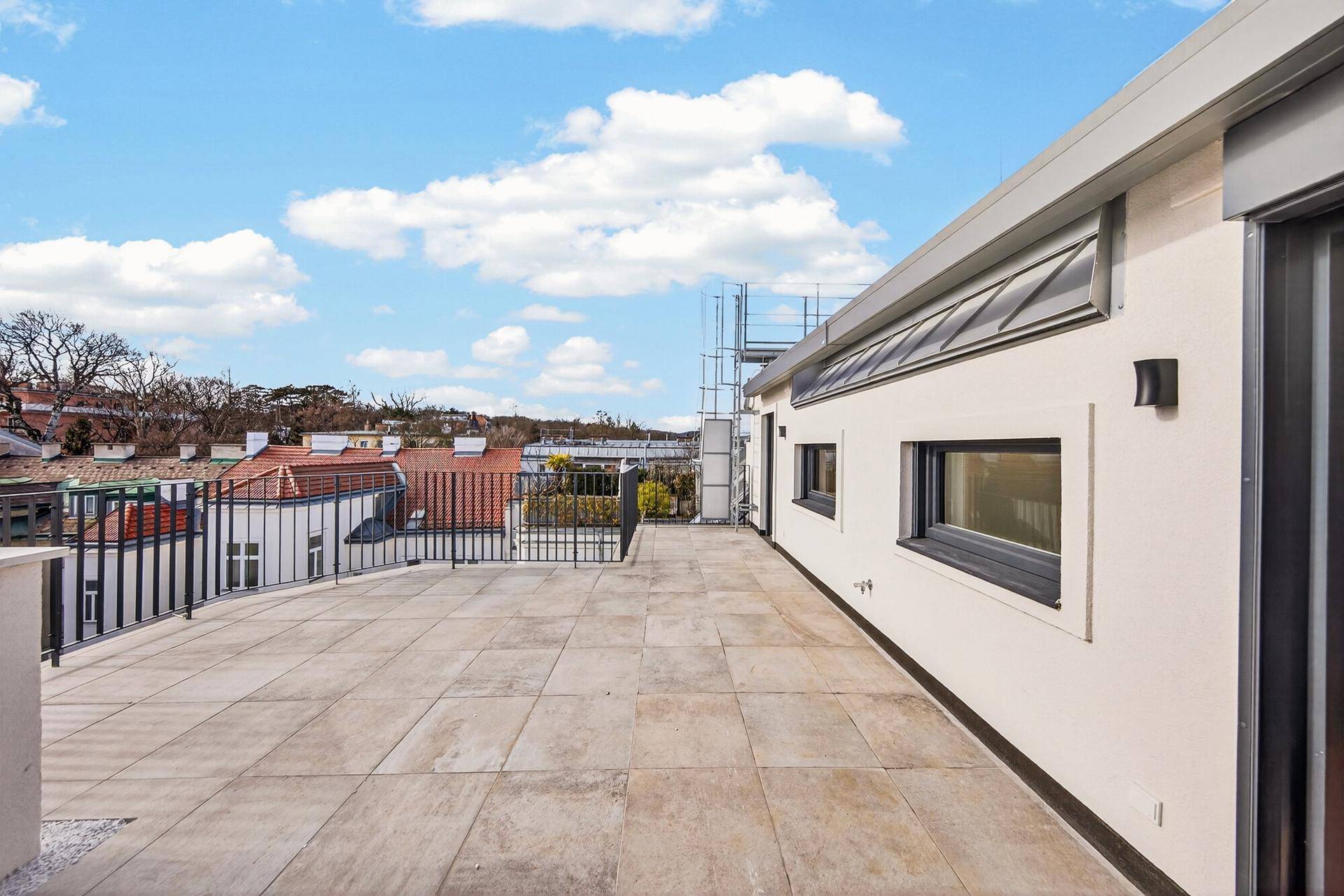 Helle, geflieste Dachterrasse entlang der Gebäudeseite mit Blick auf die umliegende Stadt.