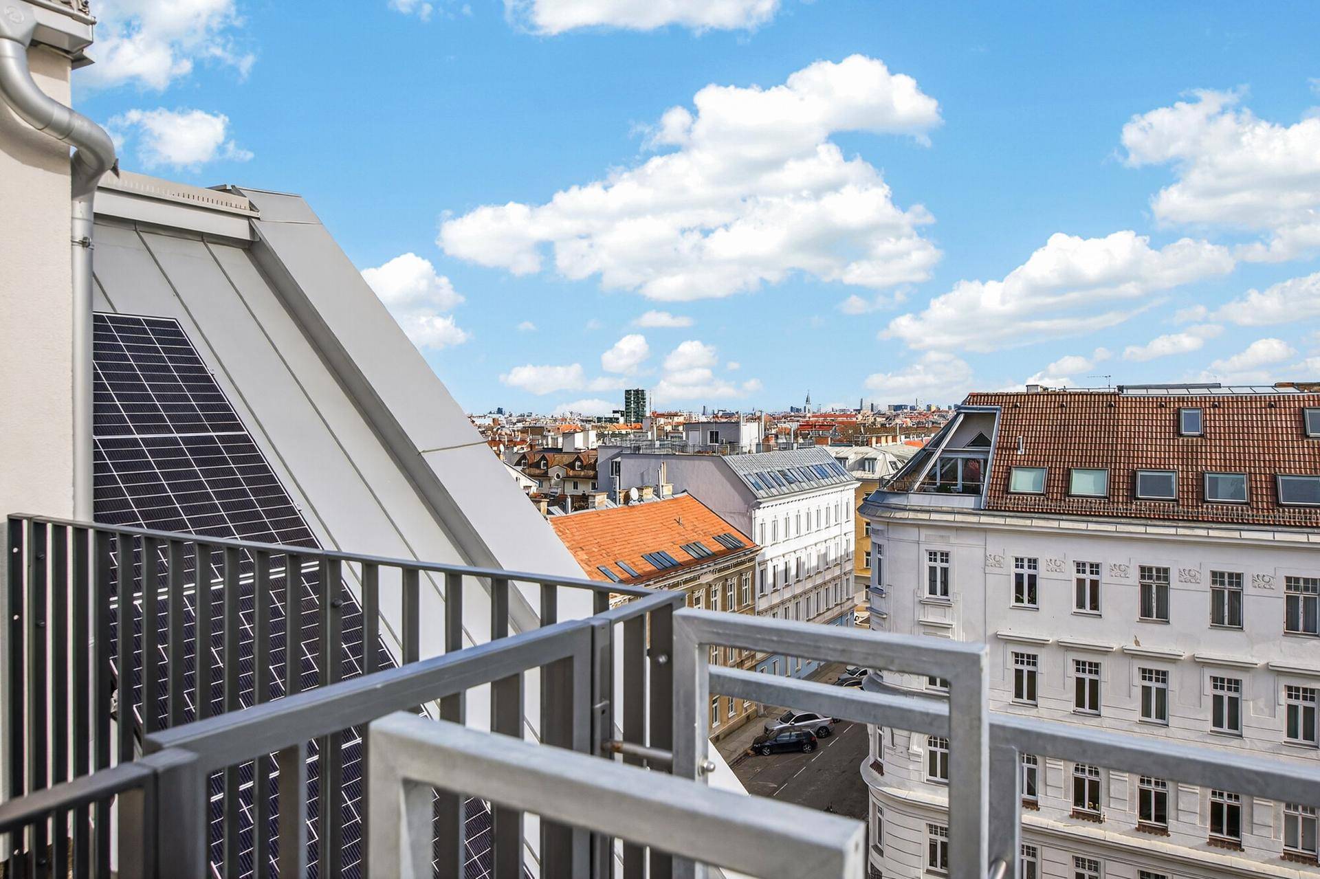 Blick von einem Balkon auf Solarpaneele auf dem Dach und die Skyline der Stadt.