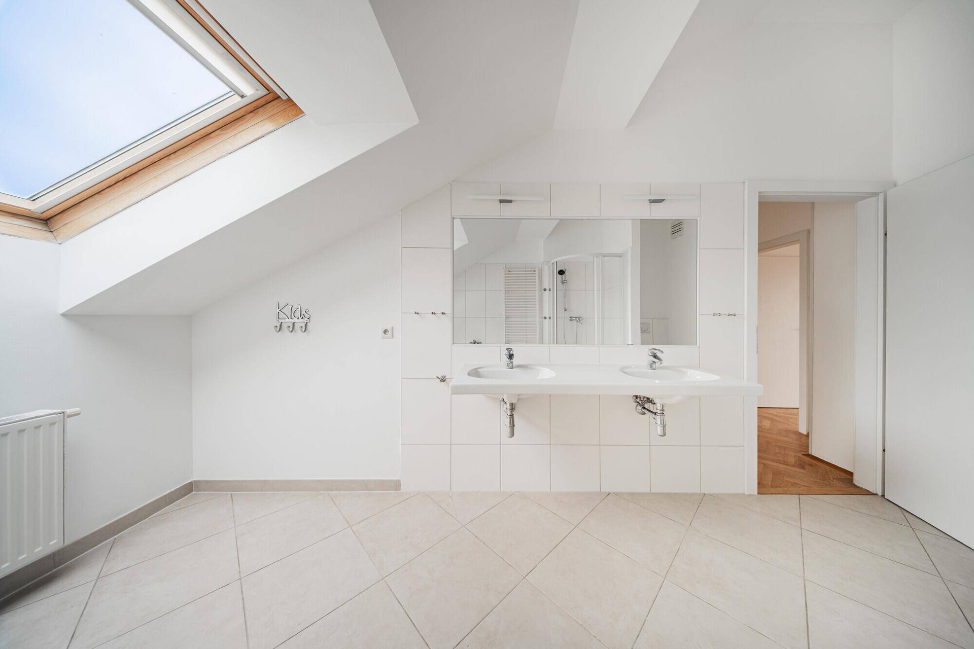 Helles Badezimmer mit Doppelwaschbecken, Fliesenboden und großem Dachfenster unter Dachschrägen.