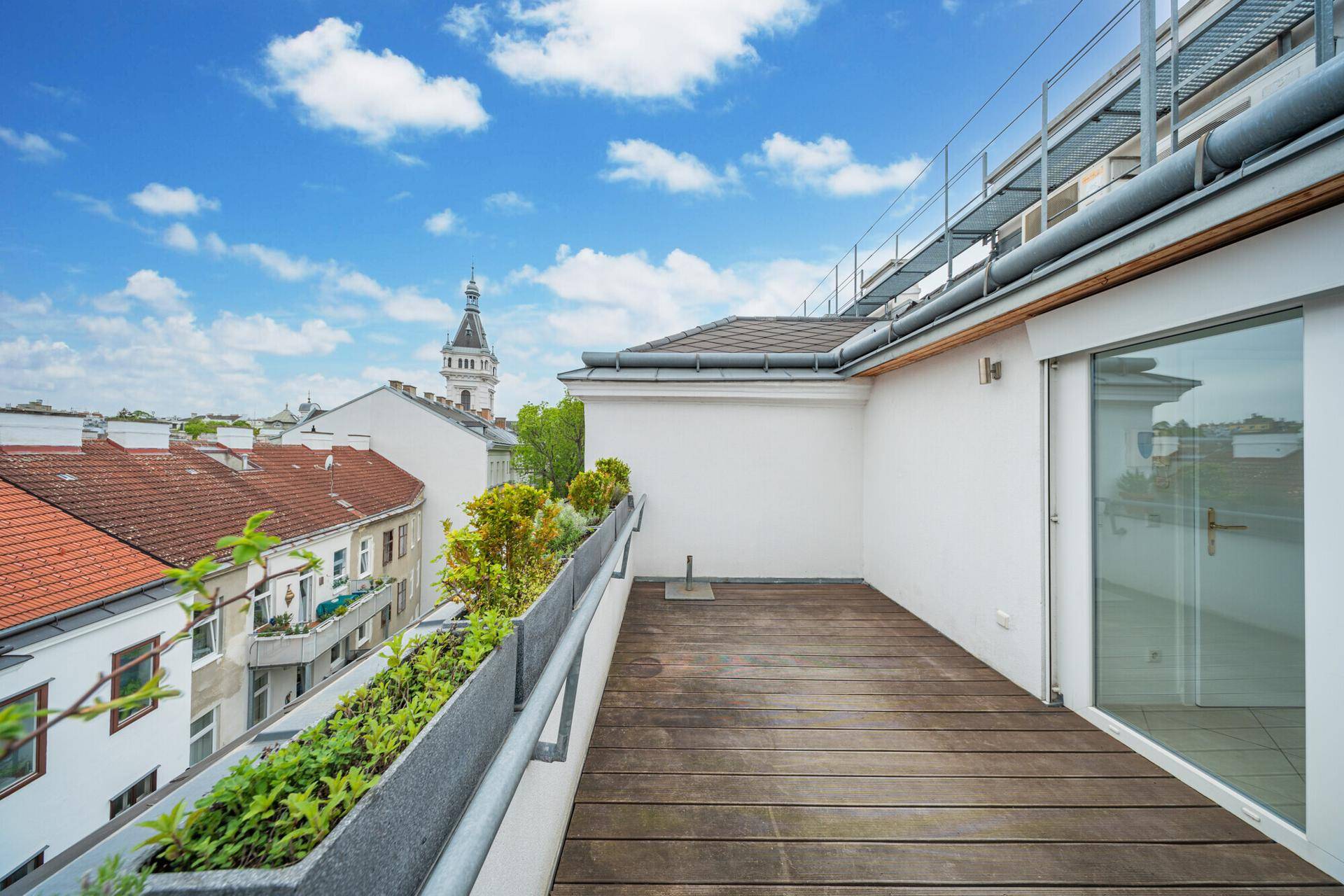 Weitläufige Dachterrasse mit Holzboden, Pflanzenkübeln und Panoramablick über die Stadt.