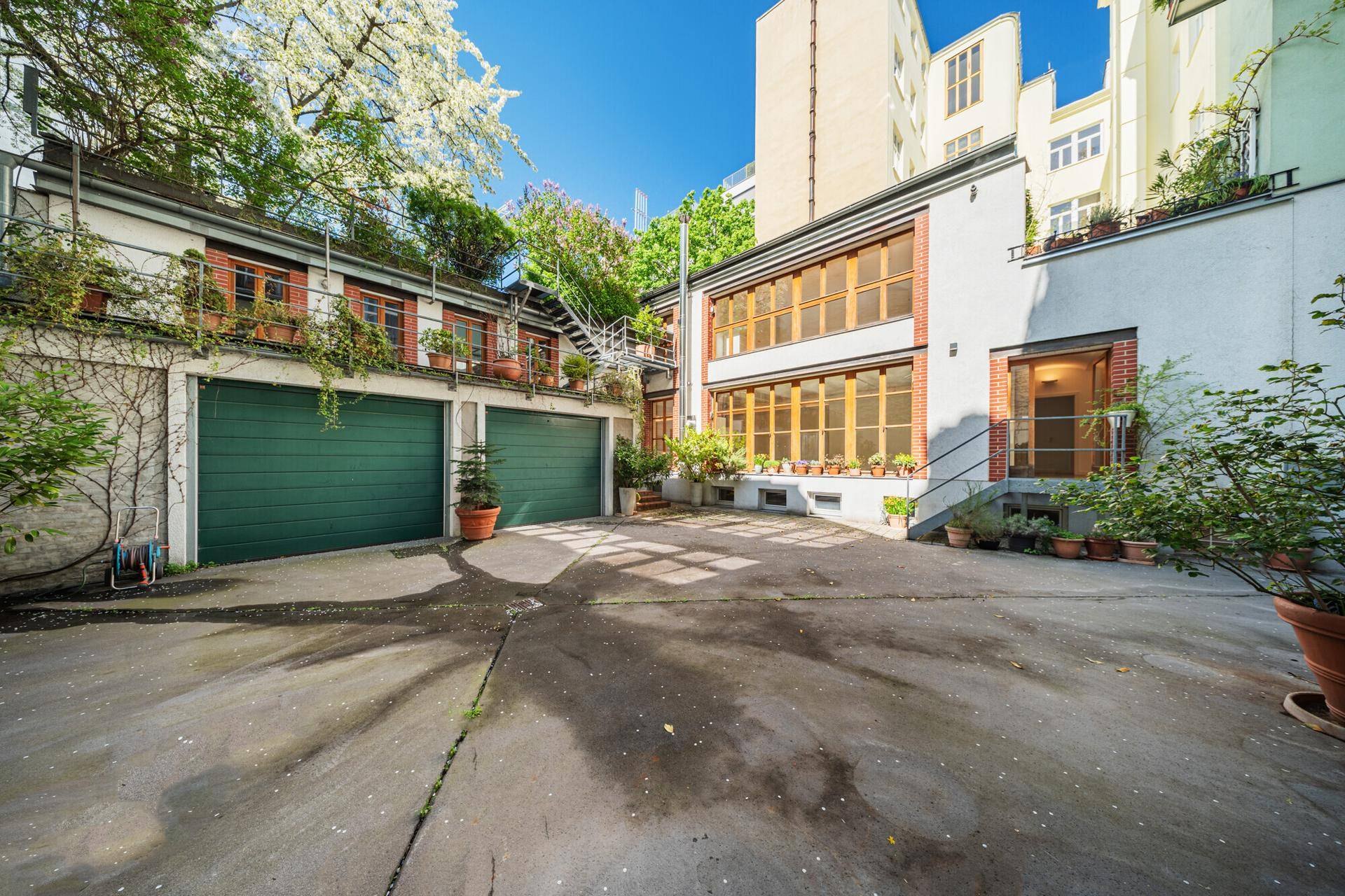 Außenansicht des Gebäudes mit zwei Garagentoren und einem gepflasterten Innenhof.