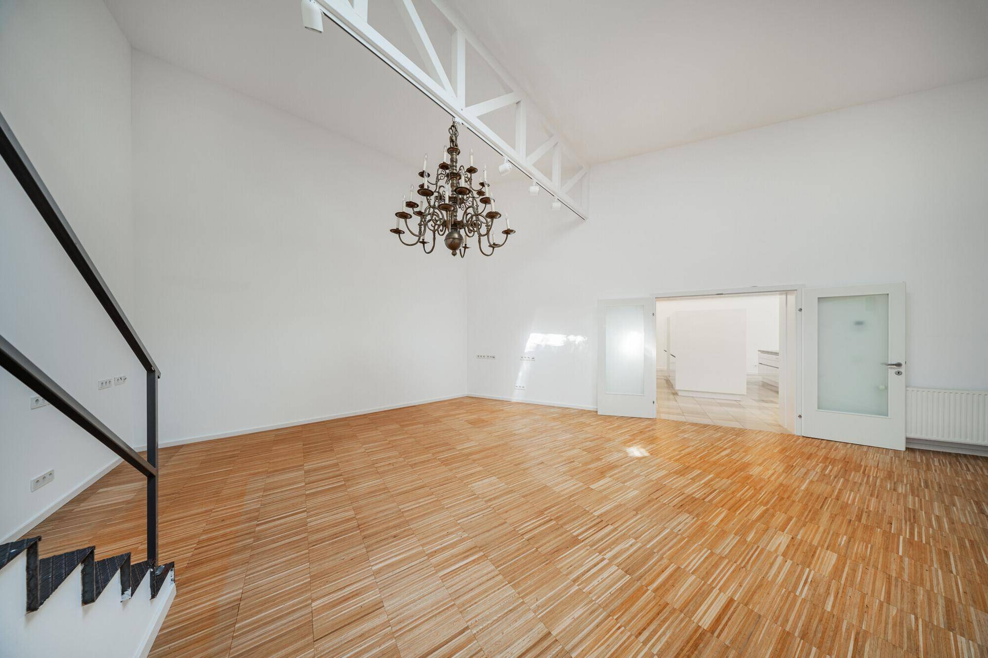 Heller Wohnraum mit hohen Decken, Parkettboden und einer eleganten Treppe zu einer oberen Ebene.