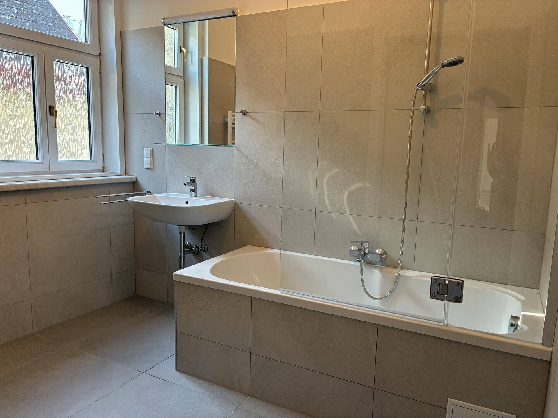 Modernes Badezimmer mit Badewanne, Waschbecken und Fenster, hell gefliest.