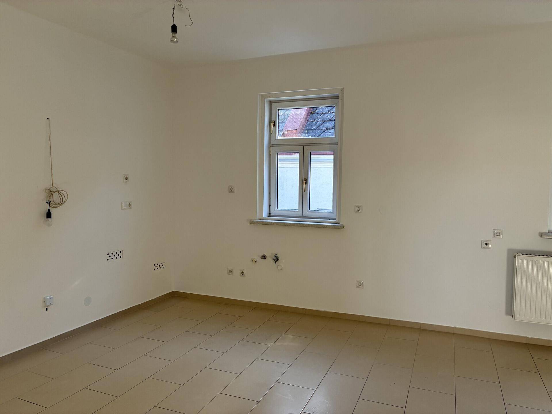 Leerer Raum mit Fliesenboden, Fenster und Heizkörper, bereit für die Gestaltung.