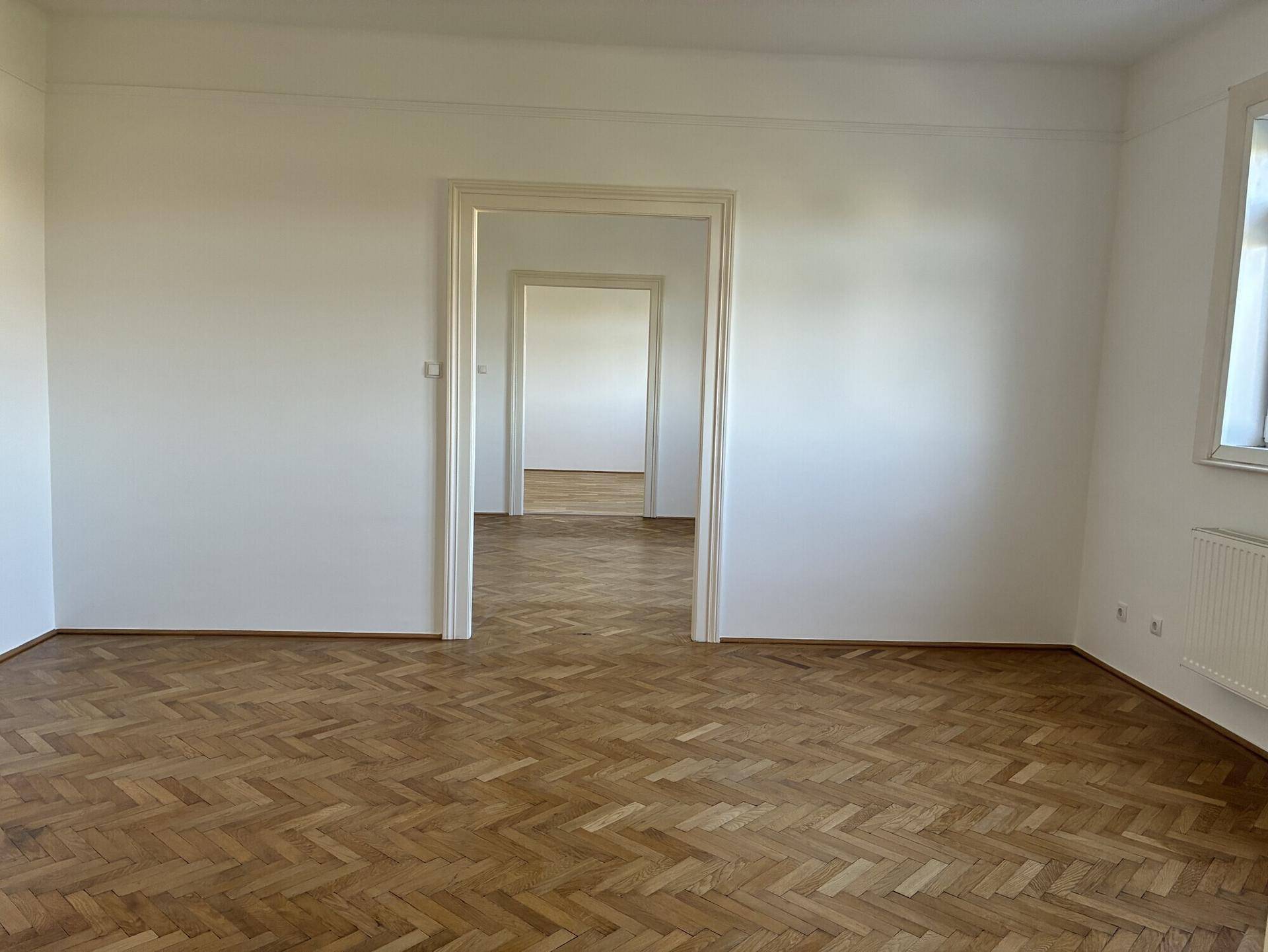 Geräumiges Zimmer mit Fischgrätparkett und mehreren offenen Türrahmen zu angrenzenden Räumen.