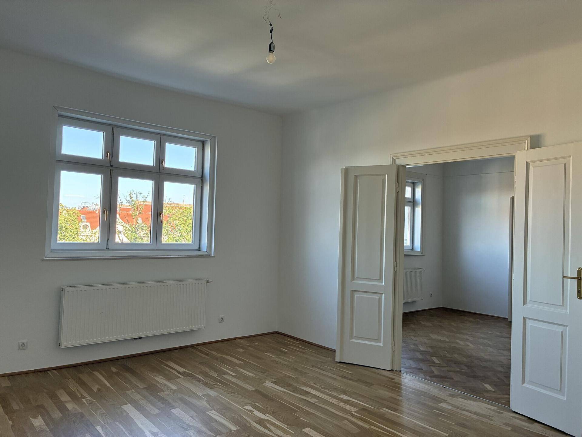 Lichtdurchflutetes Zimmer mit Holzfußboden und Fenster, das einen Ausblick bietet.
