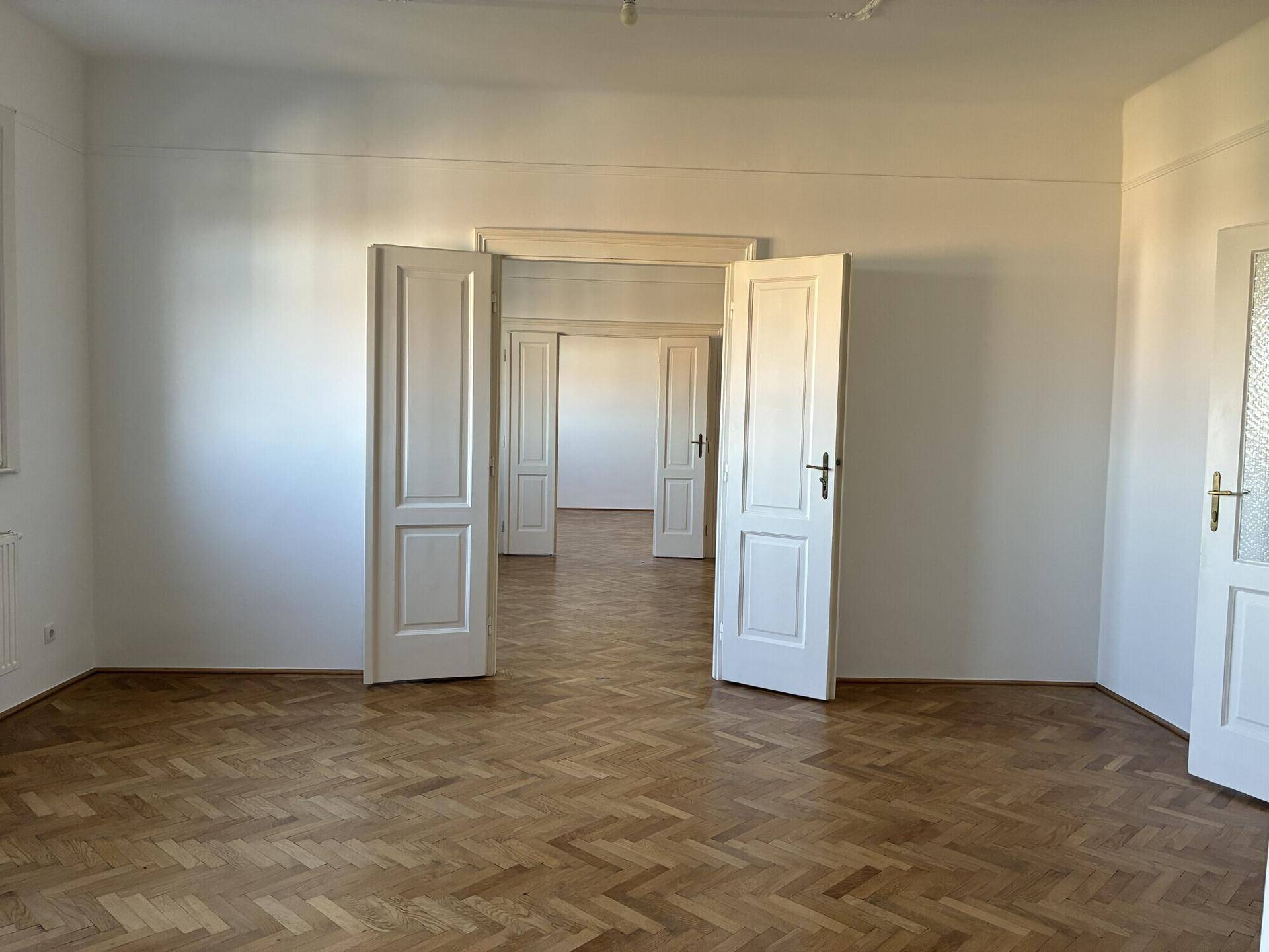 Großzügiges Zimmer mit Fischgrätparkett und vielen Türen, die eine flexible Raumgestaltung ermöglichen.