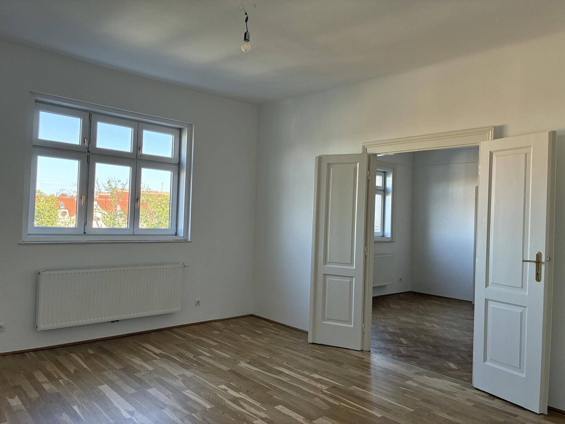 Helles Zimmer mit Holzfußboden, großem Fenster und Blick ins Grüne.