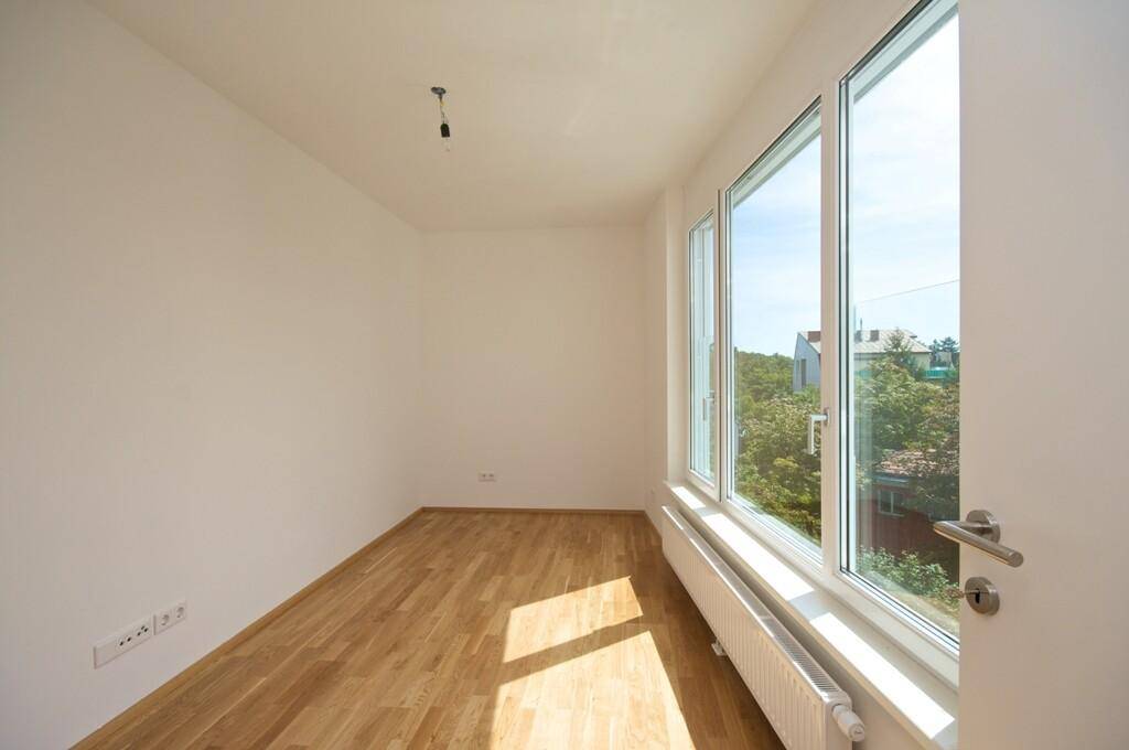 Helles Zimmer mit Parkettboden und großen Fenstern, die einen grünen Ausblick bieten.