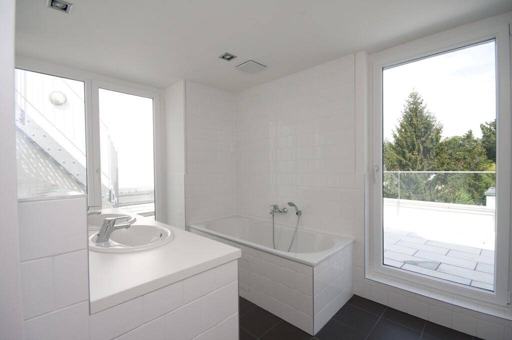 Helles Badezimmer mit Badewanne, Doppelwaschbecken und großen Fenstern mit Blick ins Grüne.