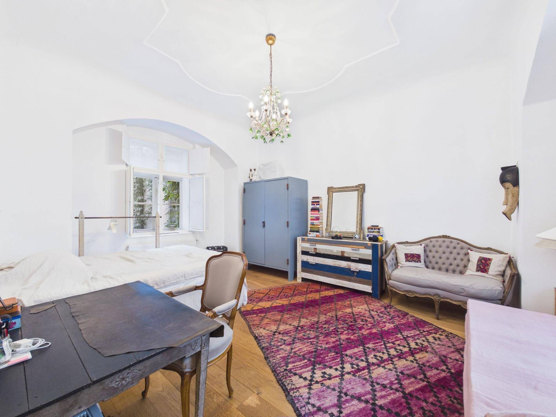Helles Schlafzimmer mit Holzboden, dekorativem Kronleuchter und einem gemütlichen Sofa.
