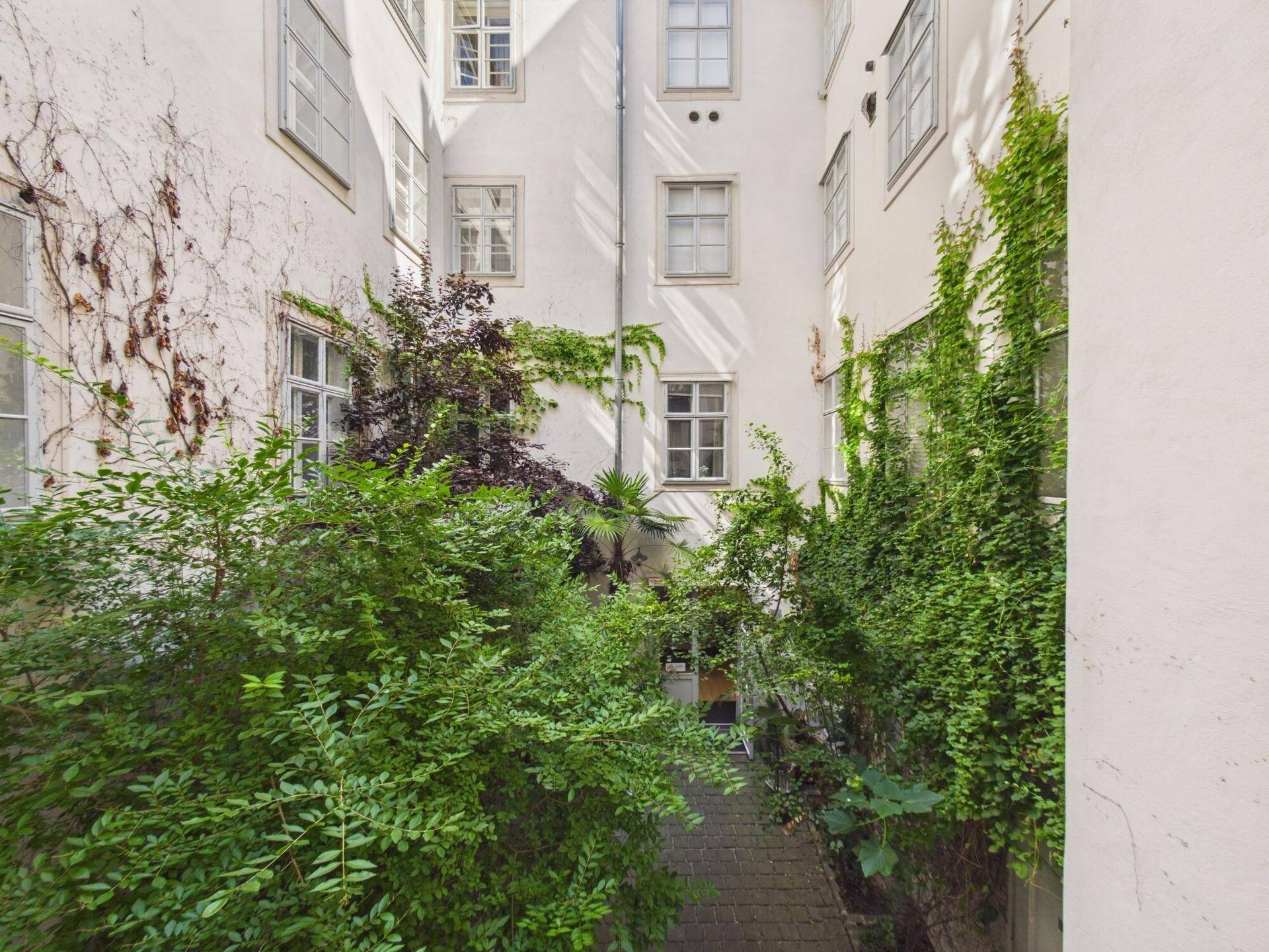 Begrünter Innenhof mit üppiger Vegetation und historischen Gebäudefassaden.