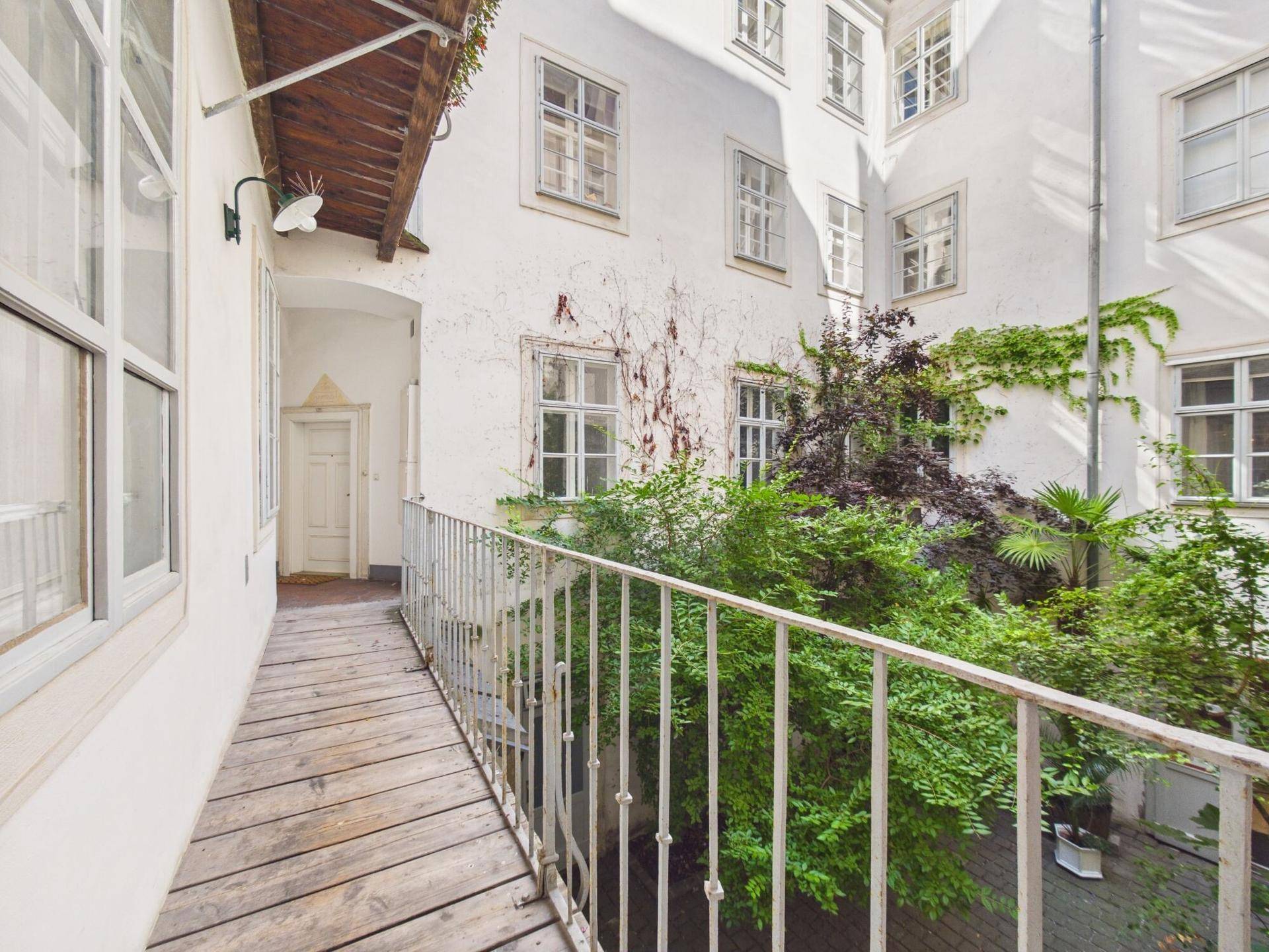 Schmaler Holzbalkon mit Metallgeländer und Blick auf den begrünten Innenhof.